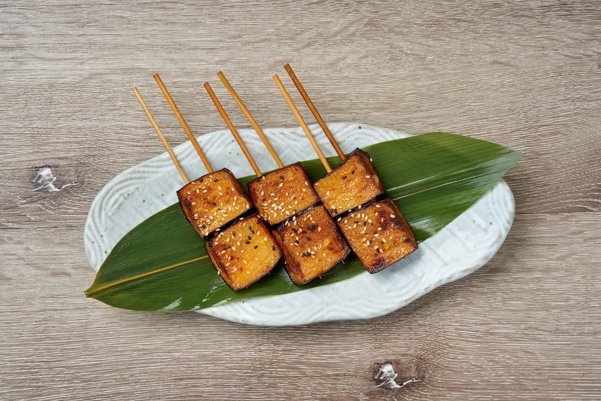Grilled skewered tofu cubes on a white plate with green leaf garnish on a wooden table