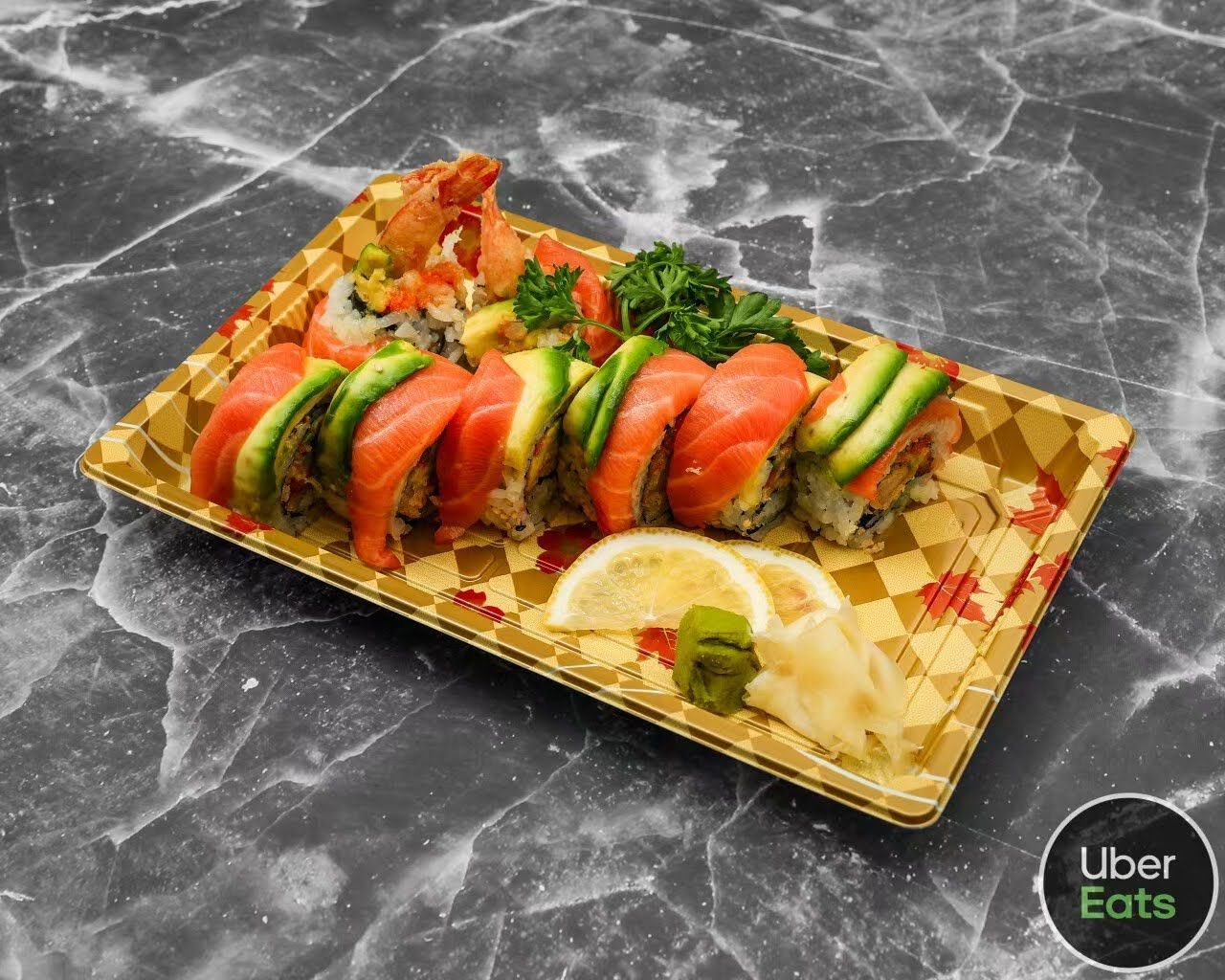 Sushi platter with salmon rolls, avocado, and dipping sauce on a gold tray
