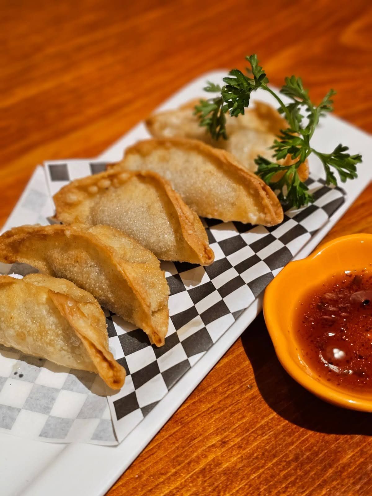Plate of fried dumplings with dipping sauce on a checkered tray, on a wooden table