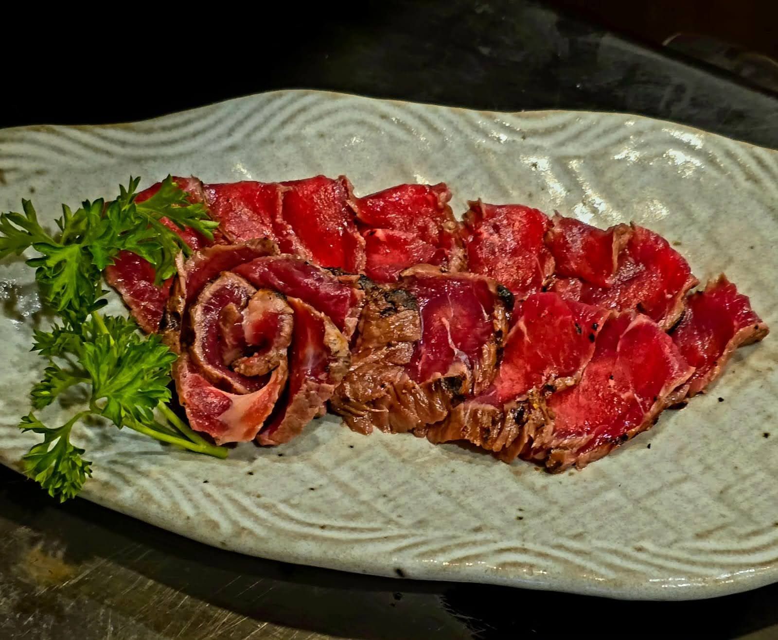 Sliced seared steak on a platter, garnished with parsley and a rolled slice of meat