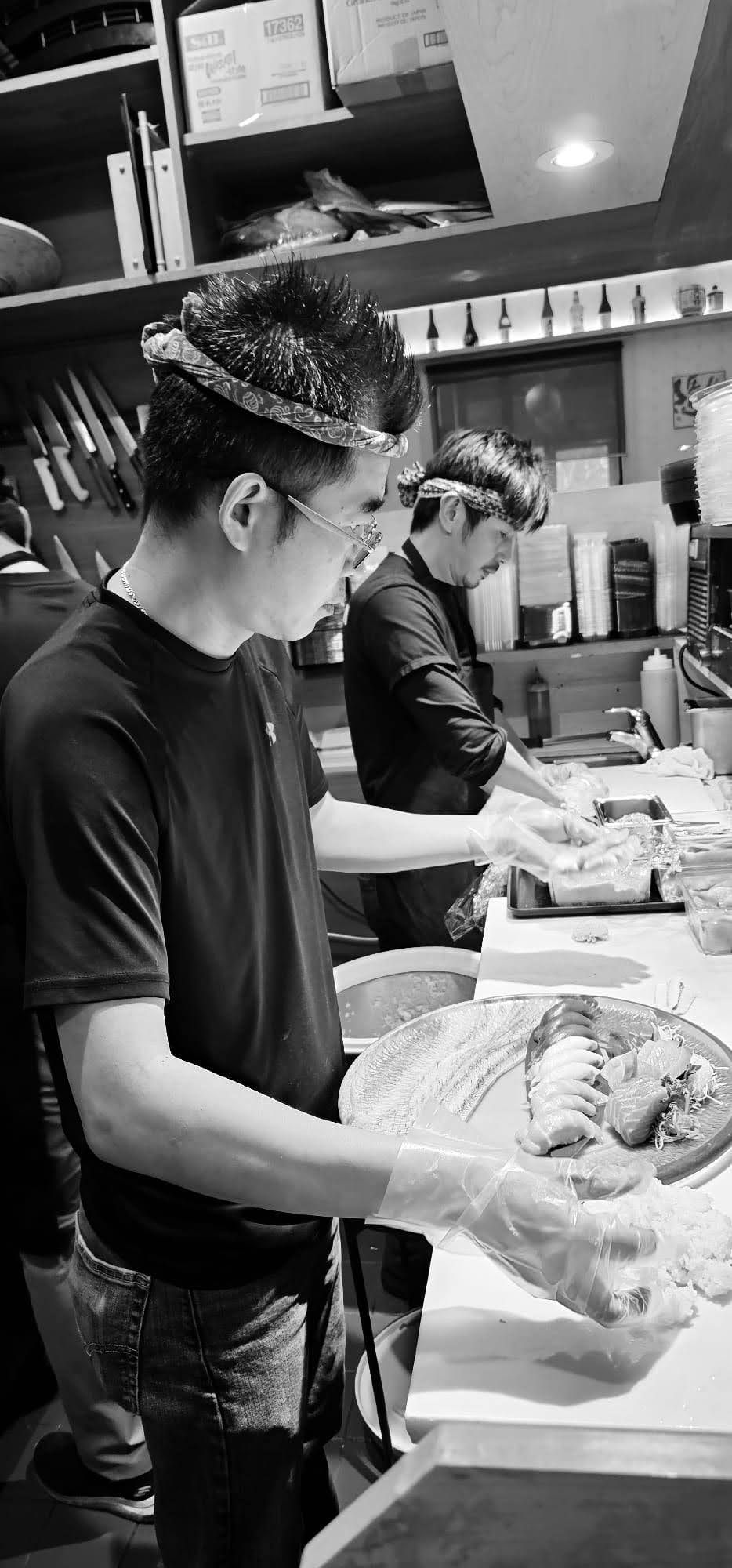 Two chefs preparing food at a kitchen counter, one plating a dish in the foreground.