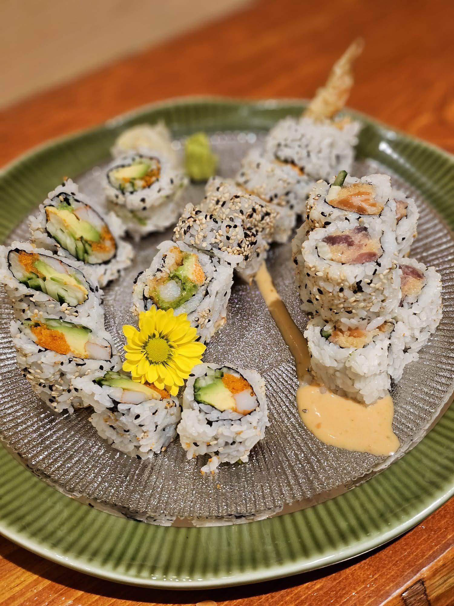 Sushi rolls on a green plate with a yellow flower garnish and dipping sauce
