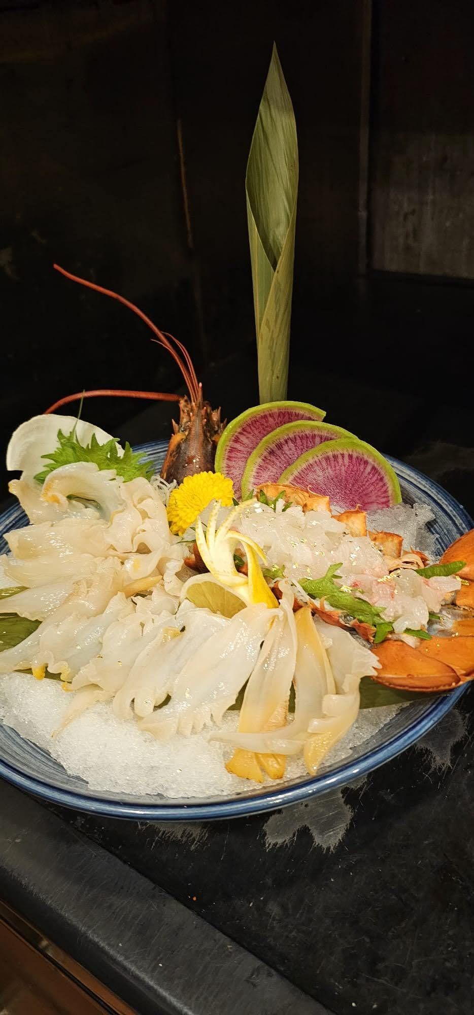 Seafood platter with shrimp, oysters, and shellfish on a black plate, garnished with lemon and herbs