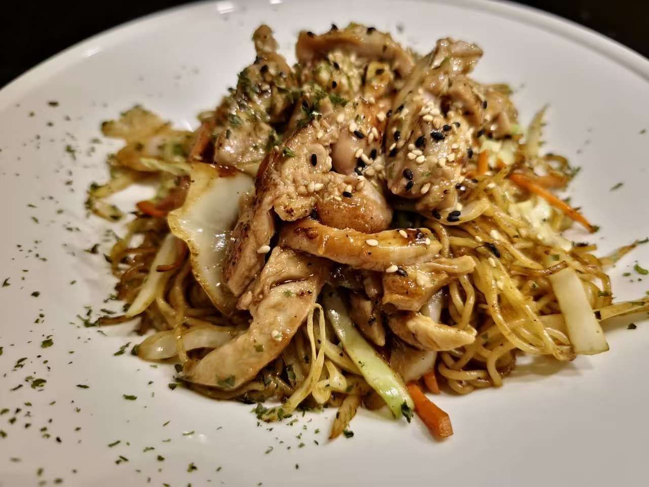 Plated noodle dish topped with sliced chicken and herbs on a white plate