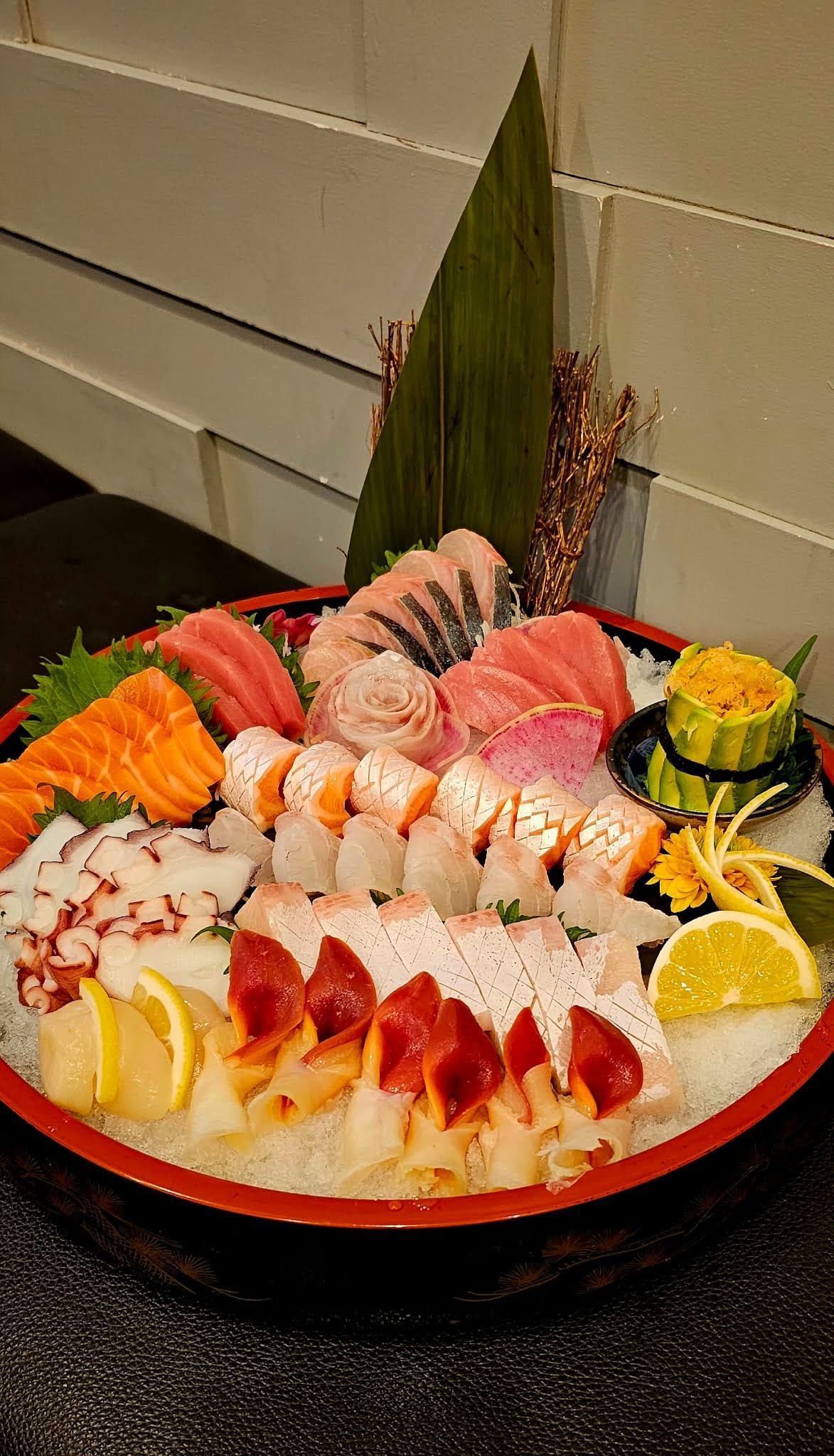 Sushi sashimi platter with assorted nigiri, rolled sushi, and lemon garnish on a red plate