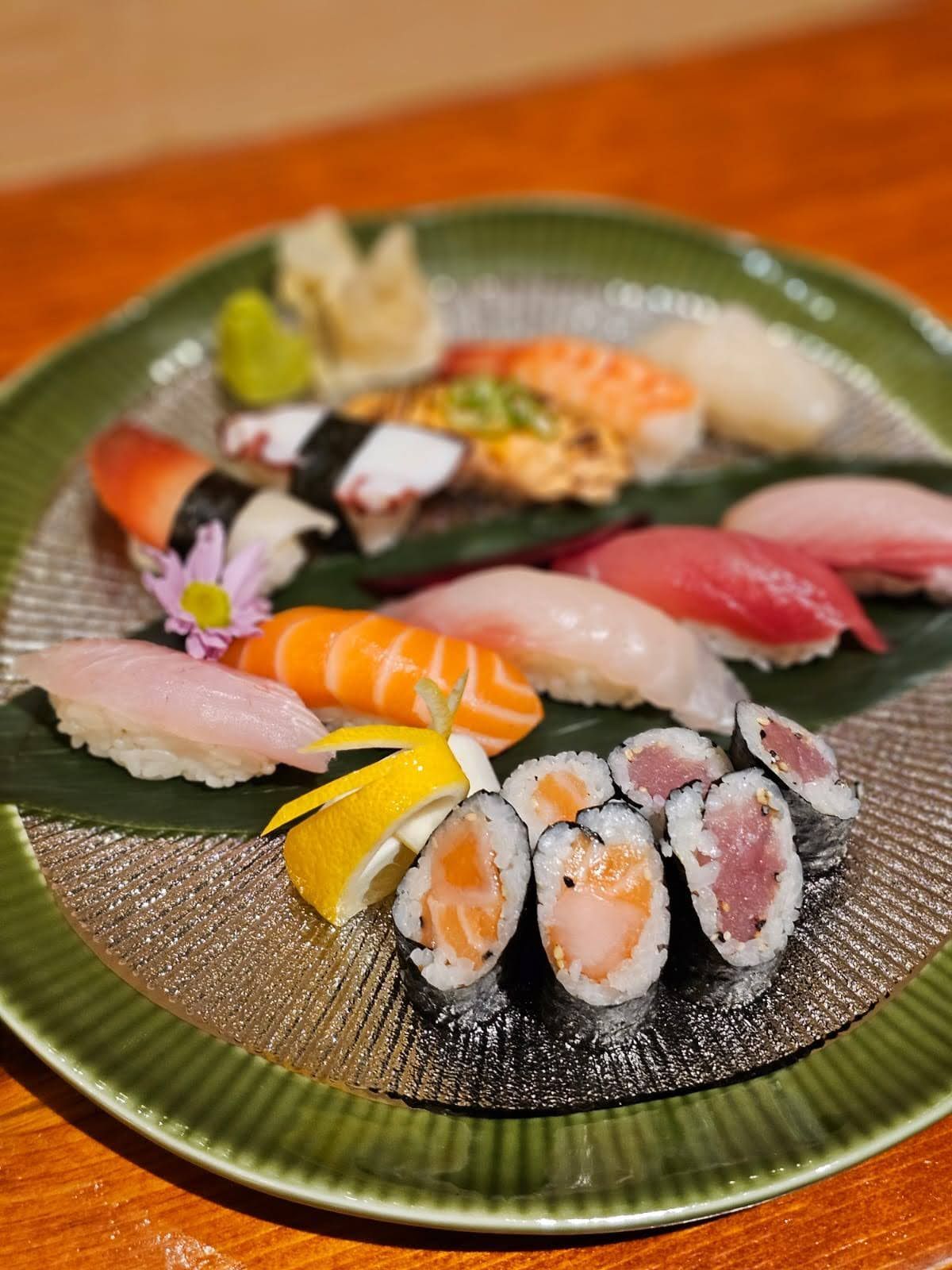 Assorted sushi on a green plate, including nigiri and rolls, with ginger and wasabi.