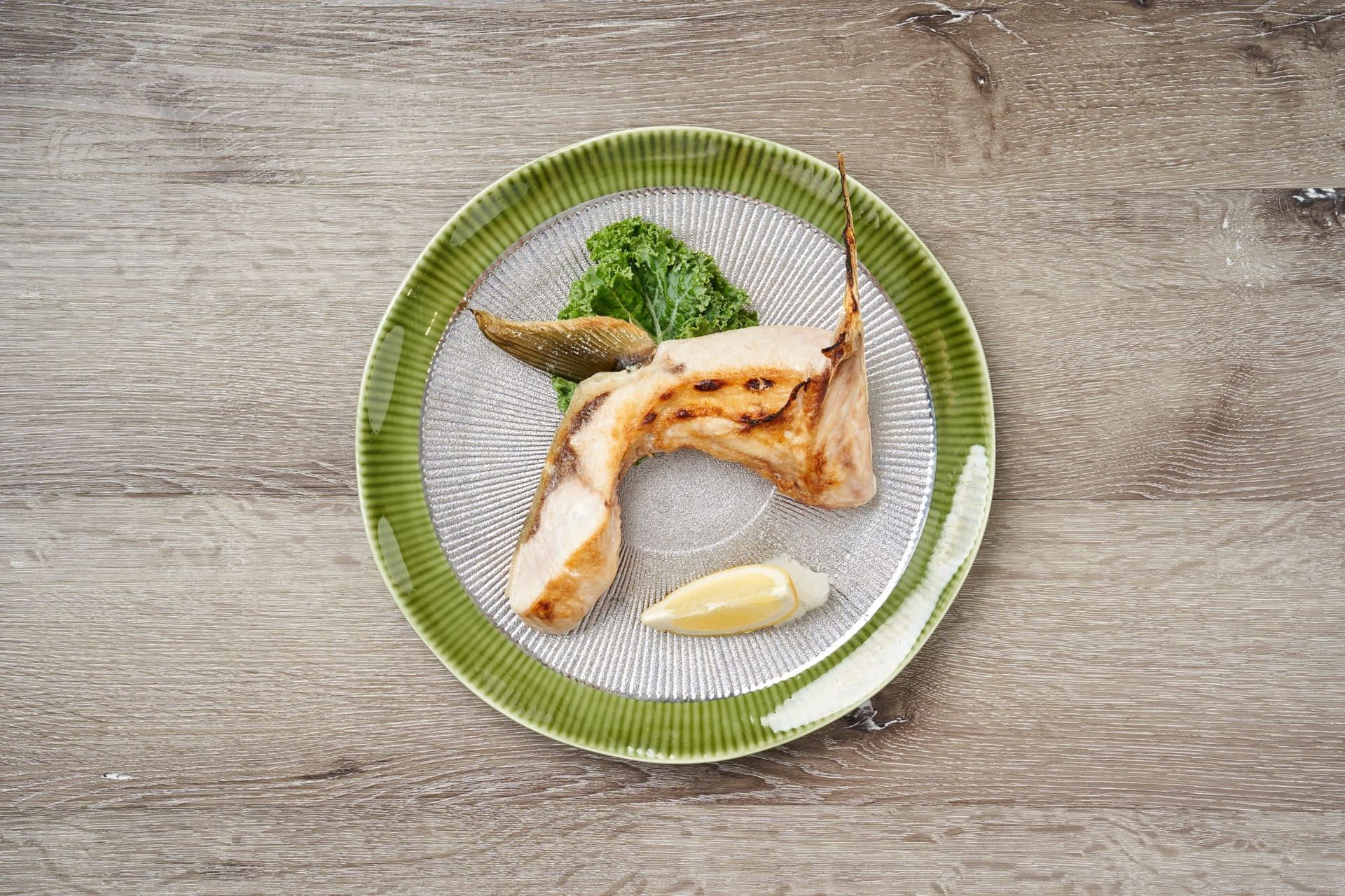 Grilled fish on a green-rimmed plate with lemon wedge and herb garnish on a wooden table