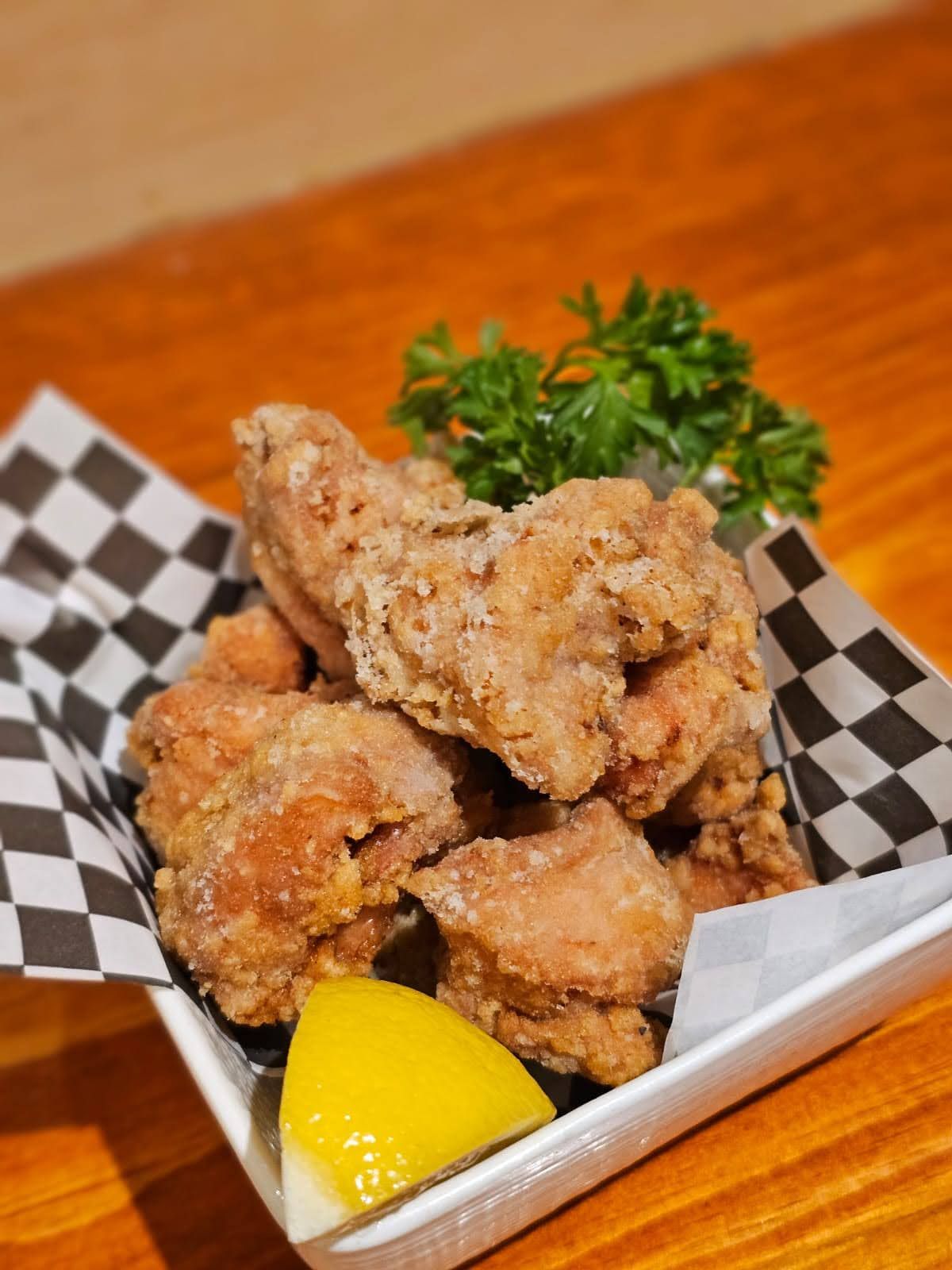 Fried chicken pieces in a checkered paper basket with a lemon wedge and parsley garnish