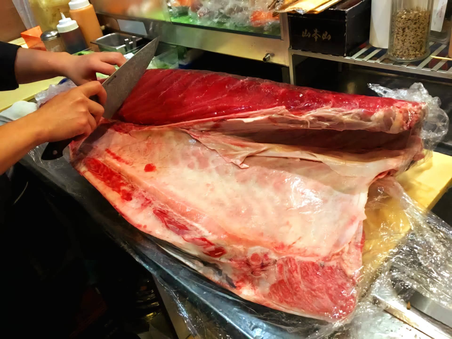 Person slicing a large red fish fillet on a market counter