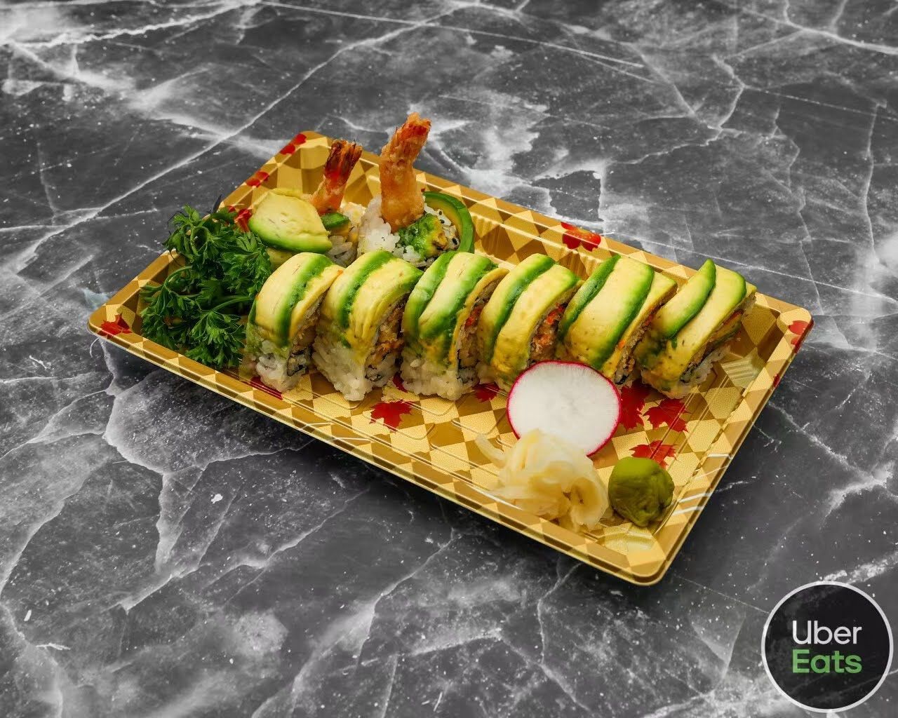 Avocado sushi roll on a gold tray with garnish, served on a dark marble table.