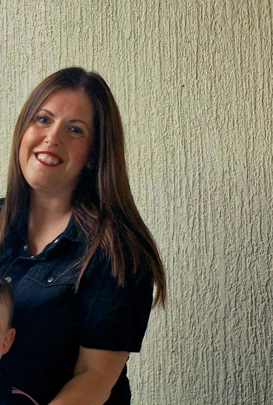 A woman in a black shirt is holding a child and smiling.