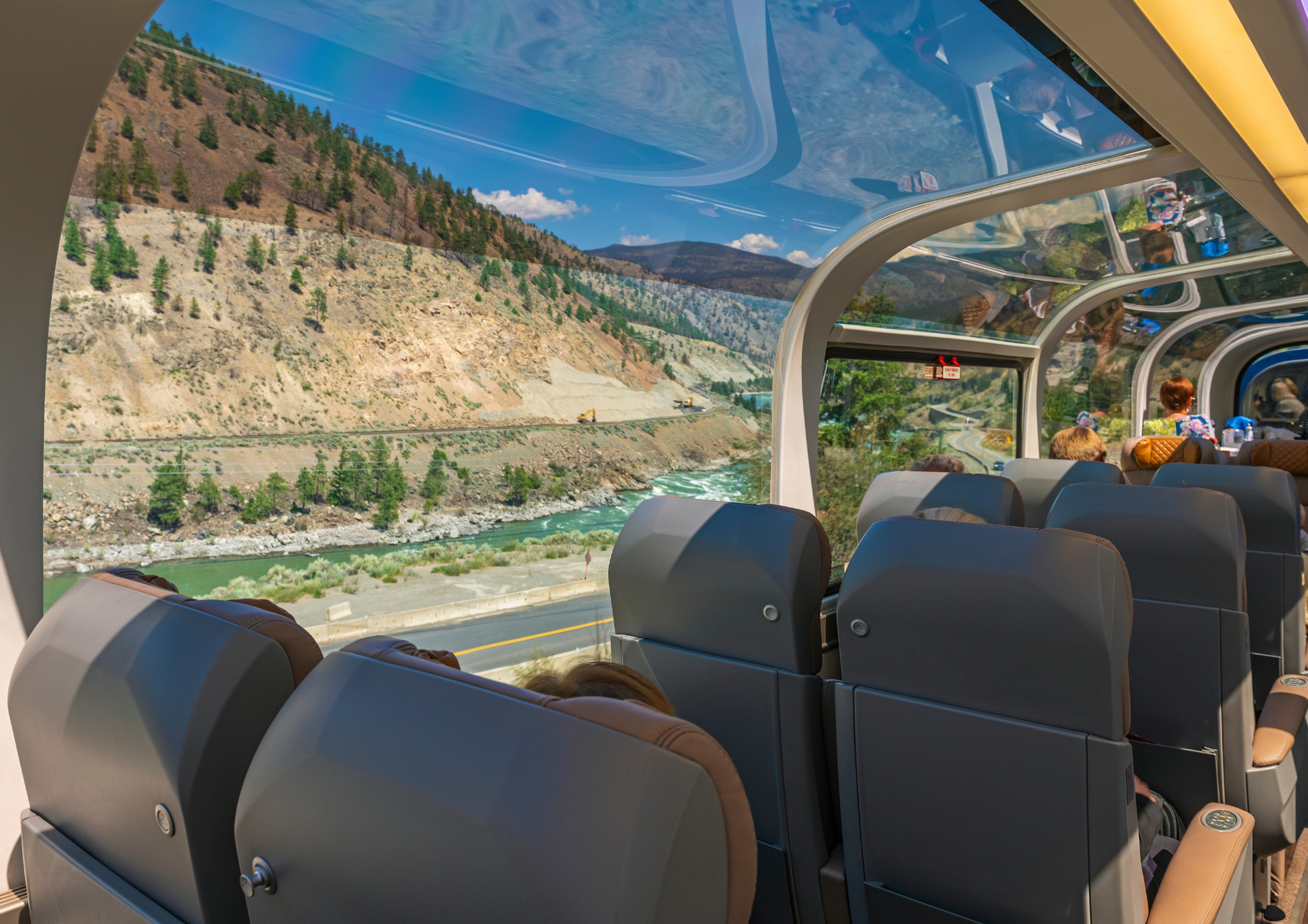 Inside a glass-topped Rocky Mountaineer overlooking a river and mountains on a sunny day