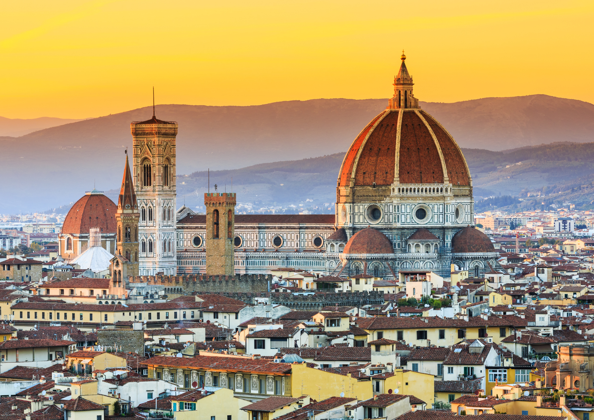 Florence skyline at sunset with the Duomo and city rooftops under warm orange light