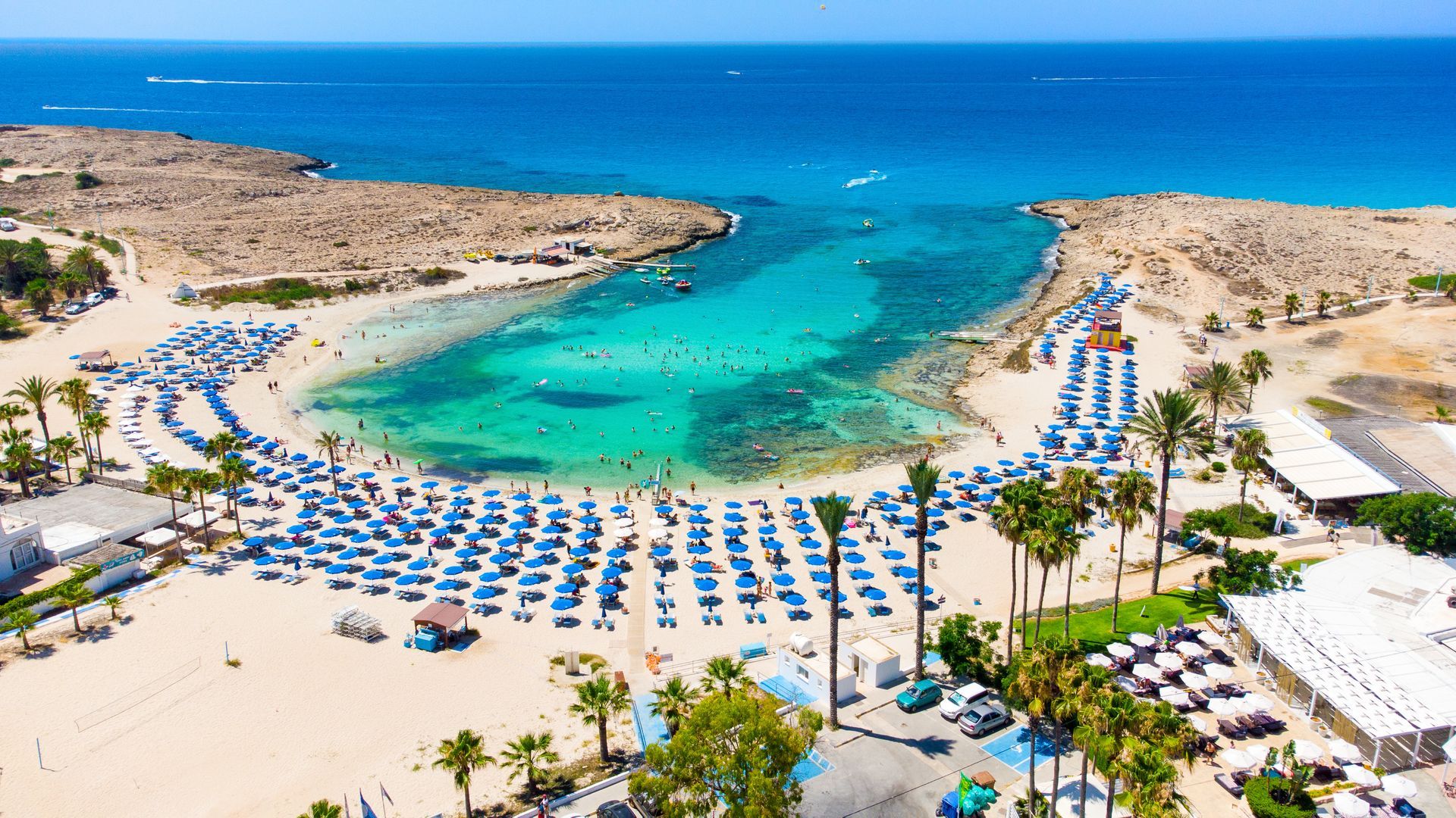 Cyprus An aerial view of a beach filled with umbrellas and palm trees next to the ocean.