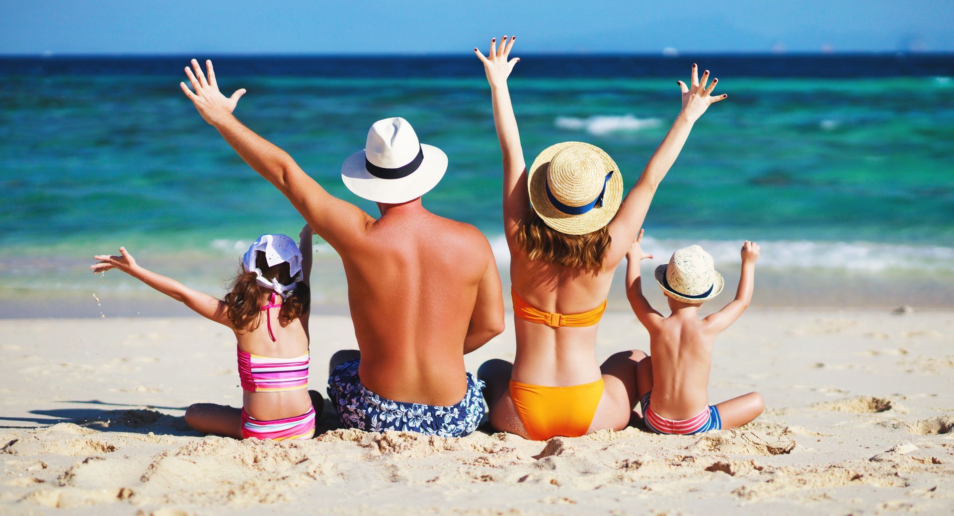 Family Holidays A family is sitting on the beach with their arms in the air.
