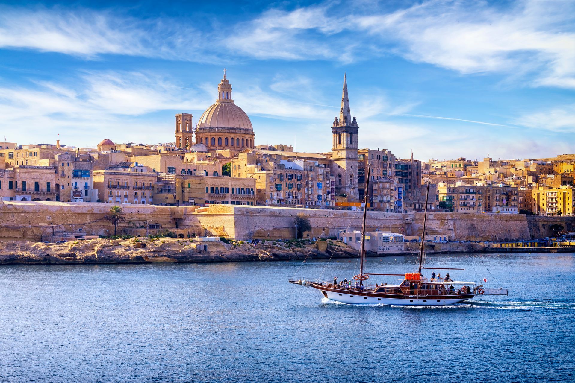 Coastal city skyline with a domed cathedral and a small boat on calm blue water at sunset