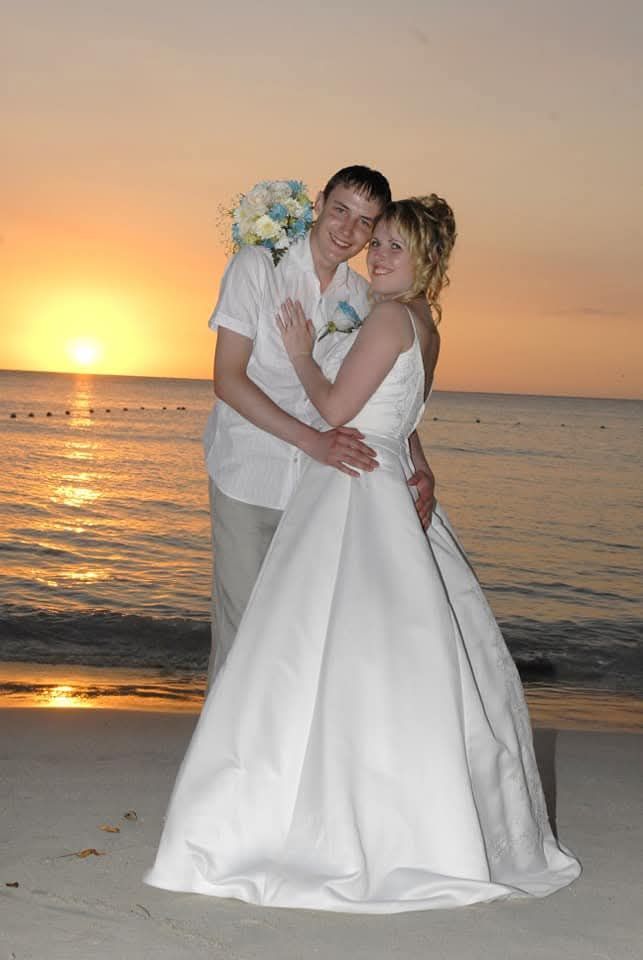 Newlyweds embracing in wedding attire on a beach at sunset