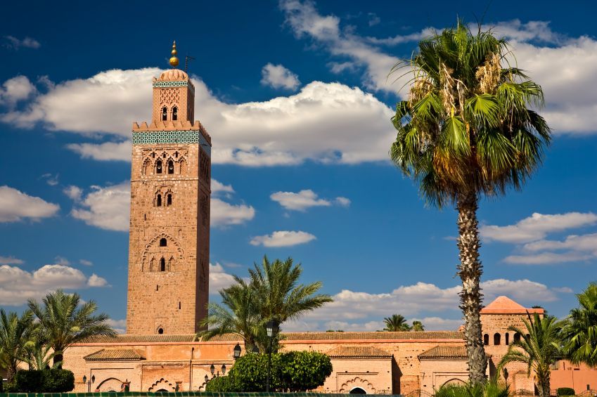 Historic brick mosque tower with a palm tree under a blue sky with clouds