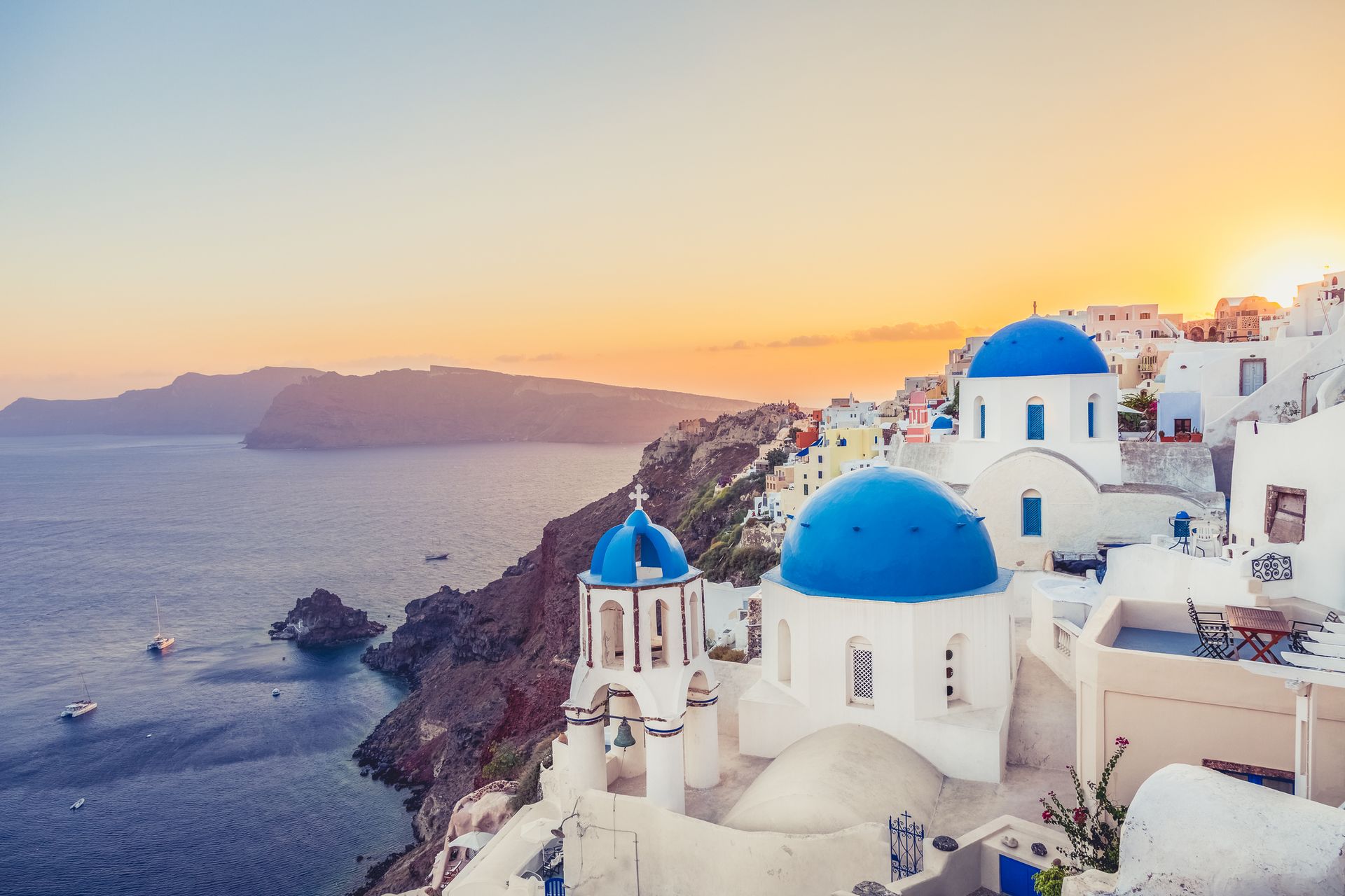 Sunset over white-and-blue cliffside buildings overlooking the sea on a Greek island