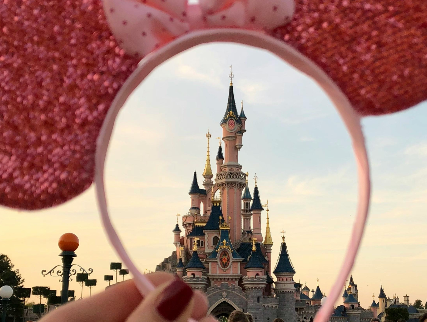 A person is holding a headband that looks like minnie mouse ears with a castle in the background