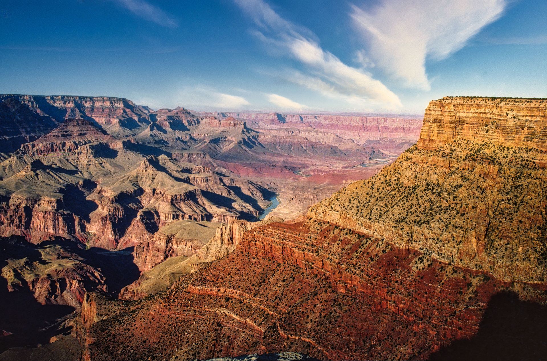Colorful Grand Canyon cliffs and mesas under a blue sky with wispy clouds