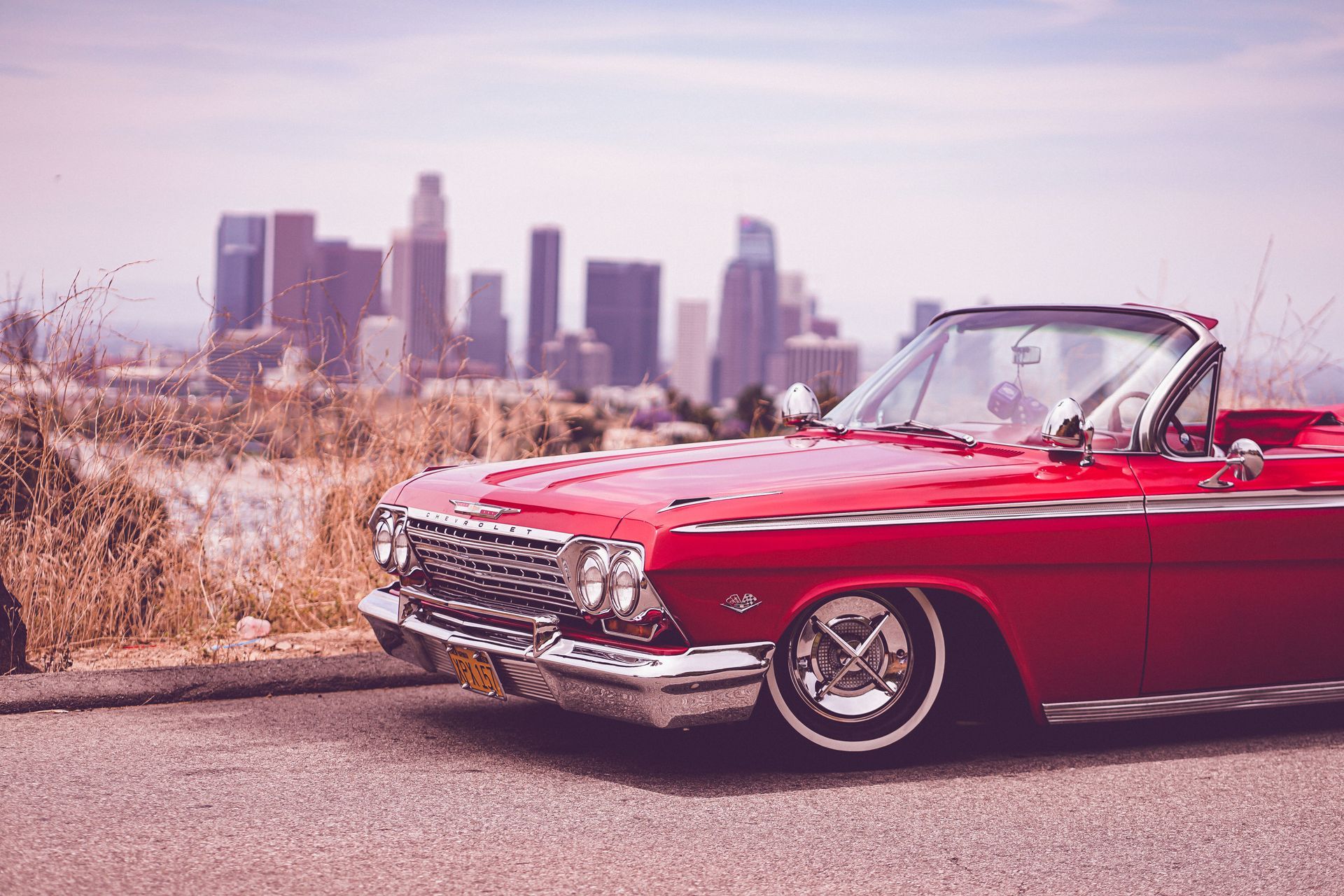 Red vintage convertible parked roadside with a city skyline in the background