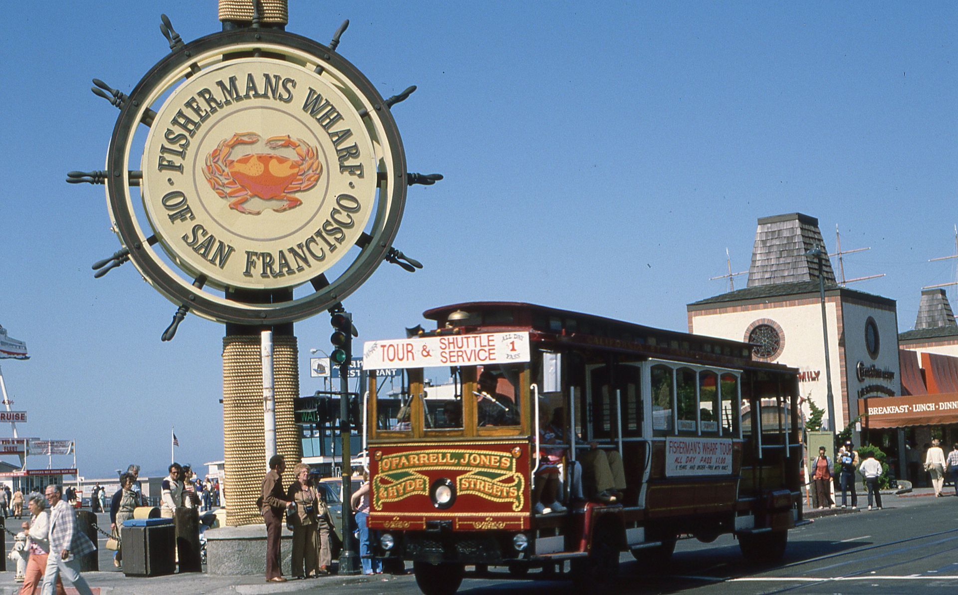 Cable car at Fisherman's Wharf, San Francisco, beside a large round sign on a sunny day