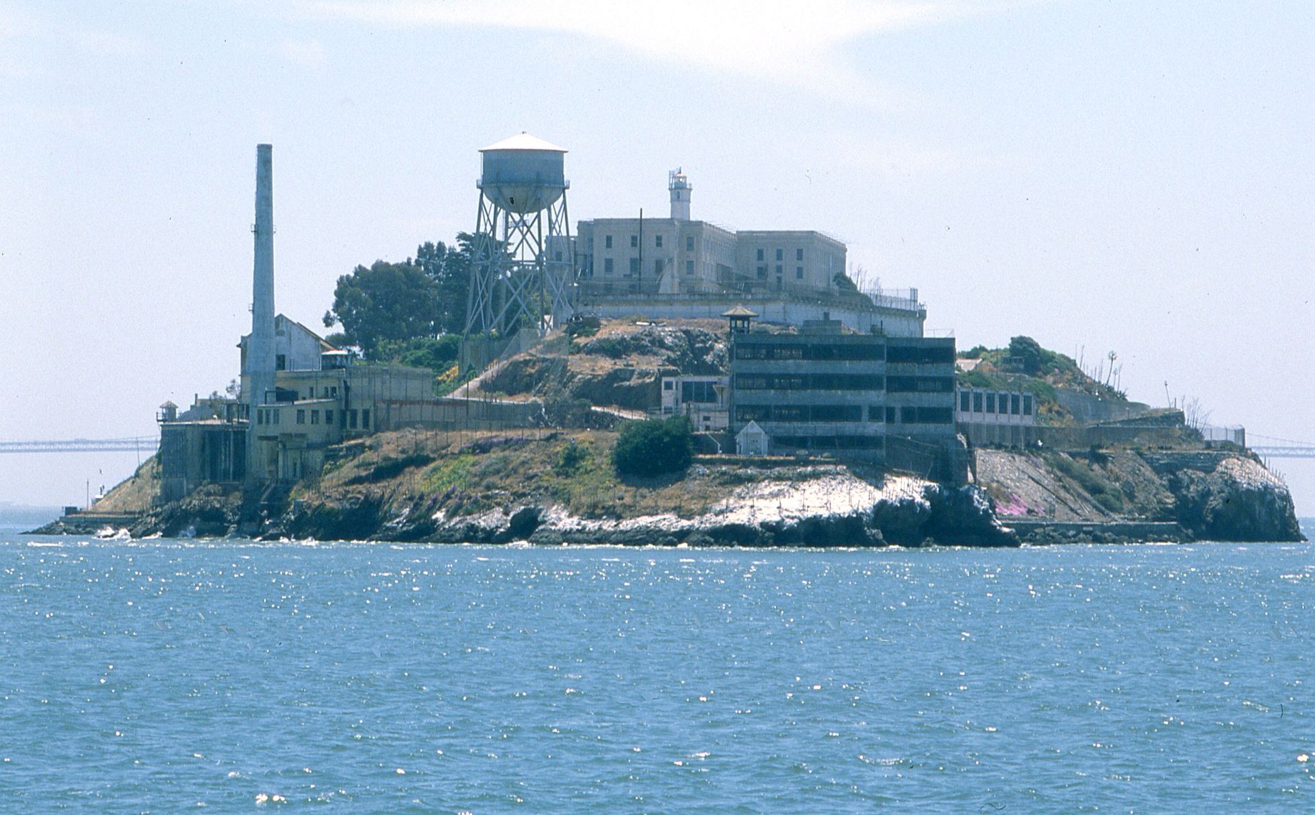 Famous Alcatraz island prison surrounded by ocean, with concrete buildings and a water tower.