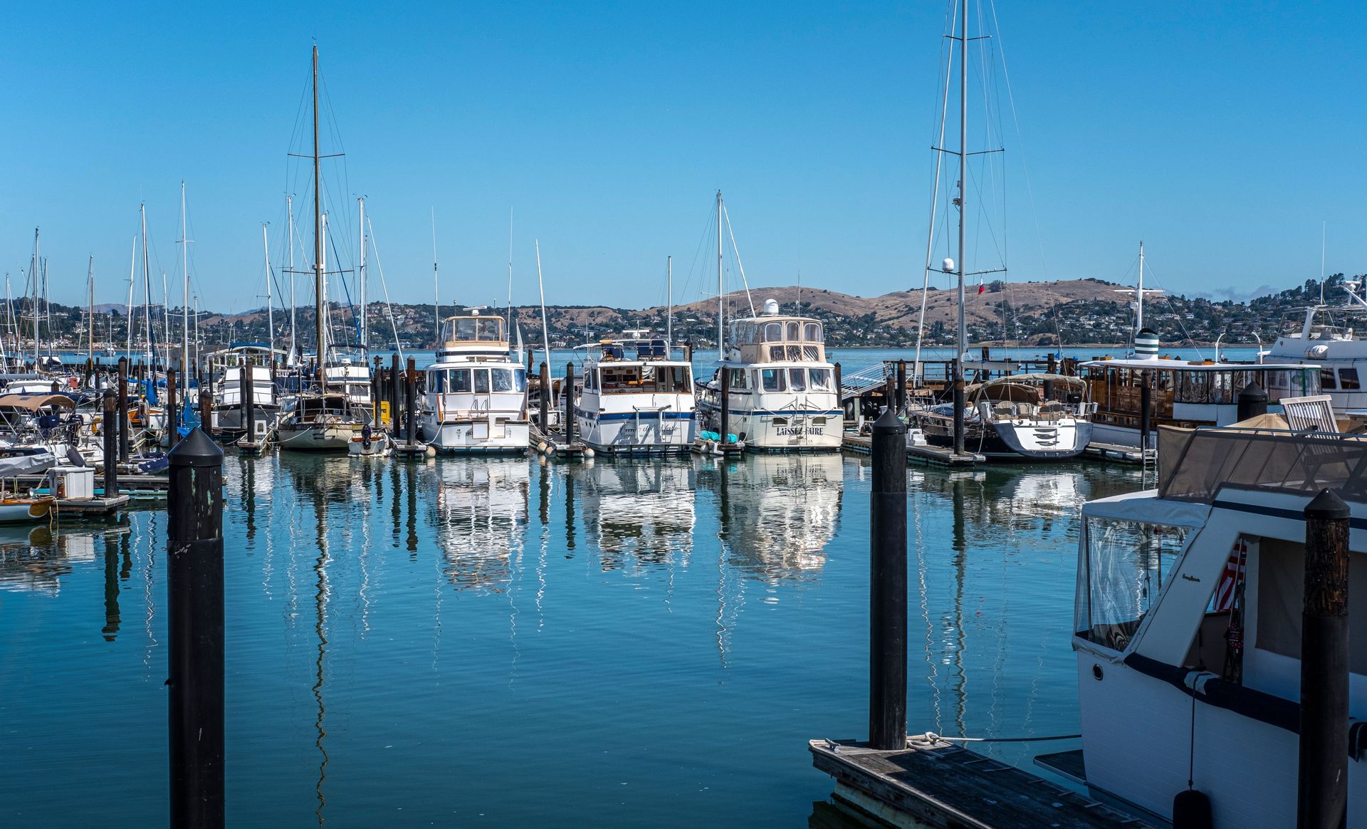 Marina with docked sailboats and yachts on calm blue water under a clear sky