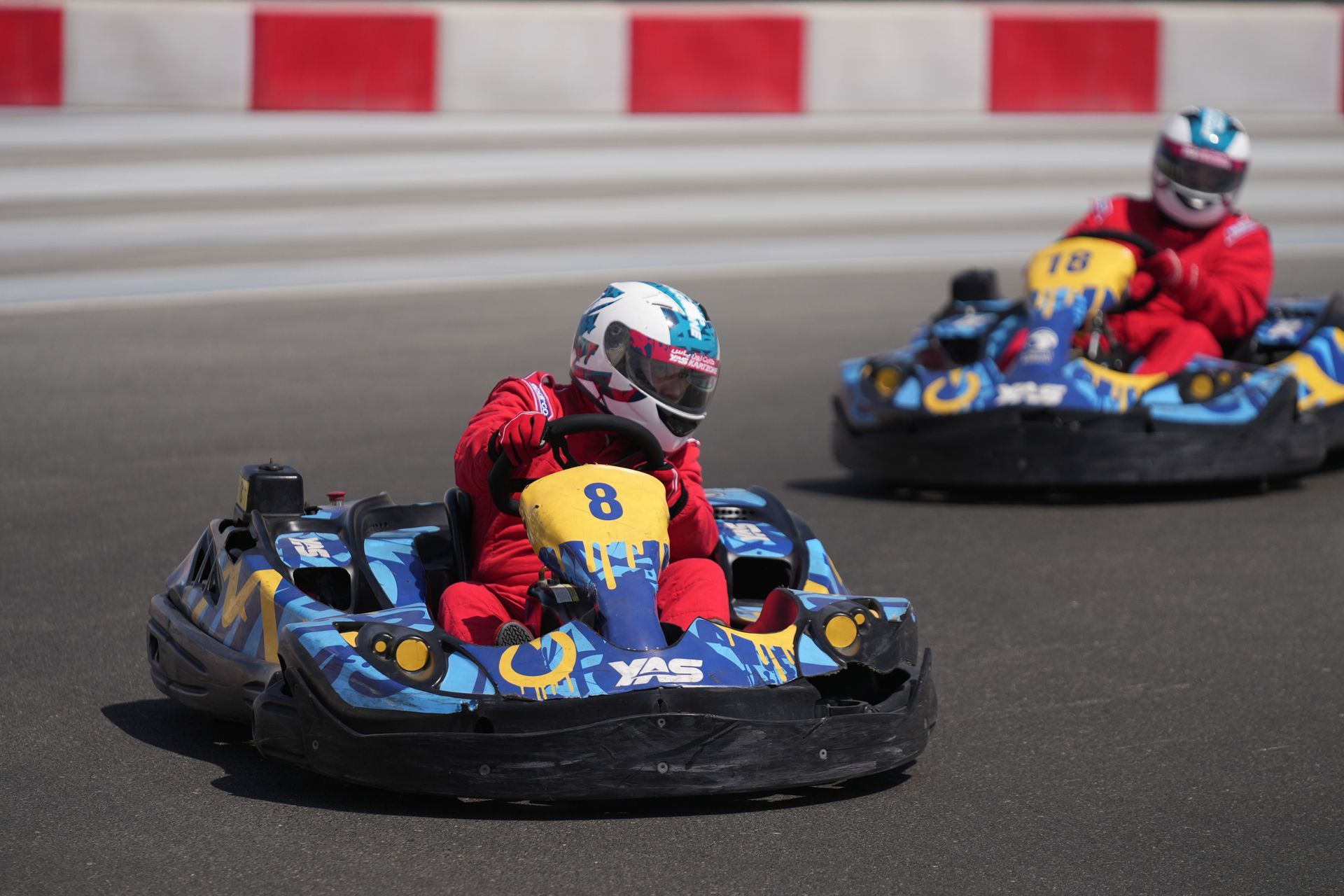 Two go-karts racing on a track, drivers in red suits, front kart leading around a turn