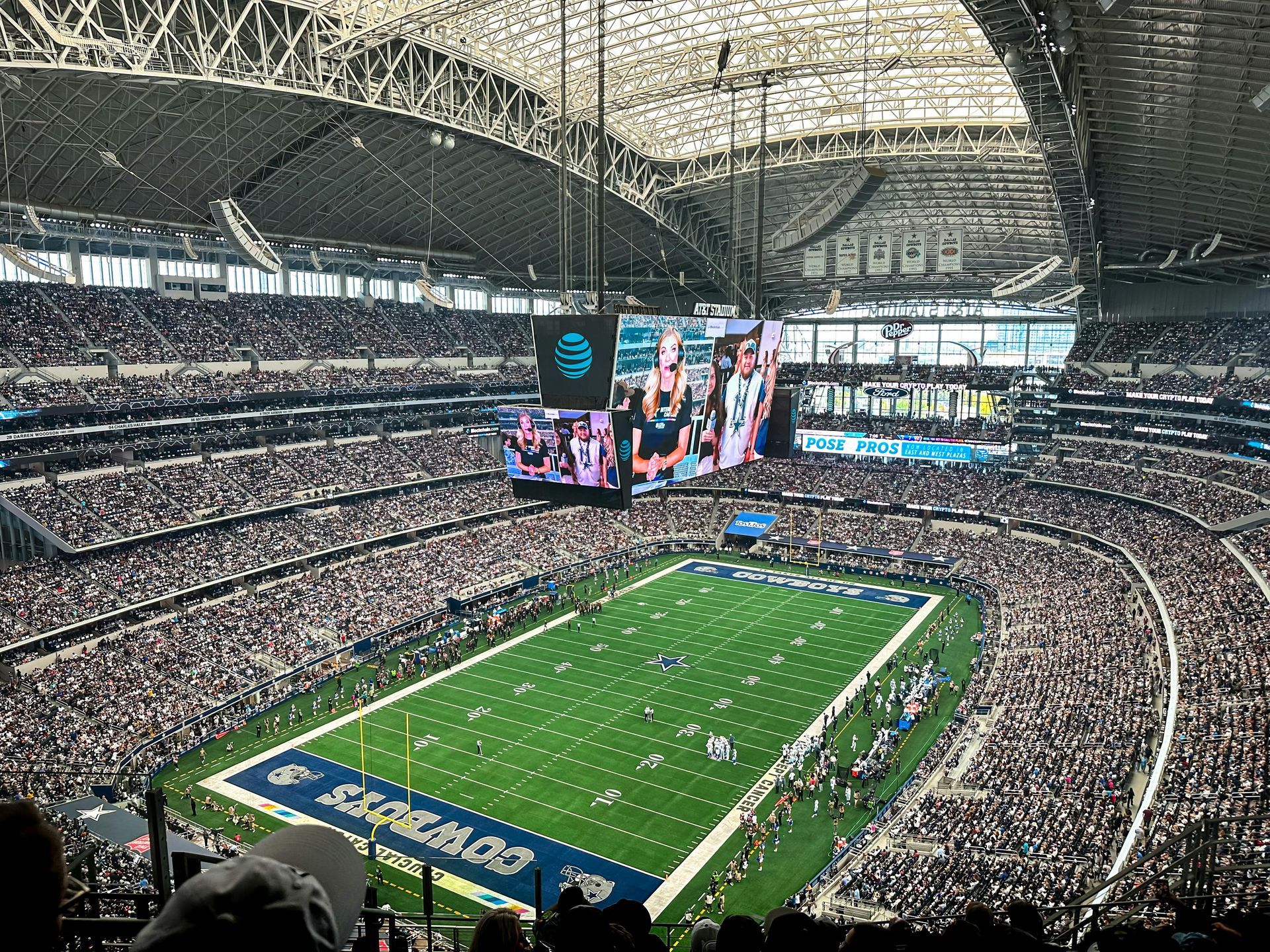 Indoor football stadium packed with fans, with a green field and large video screens overhead.
