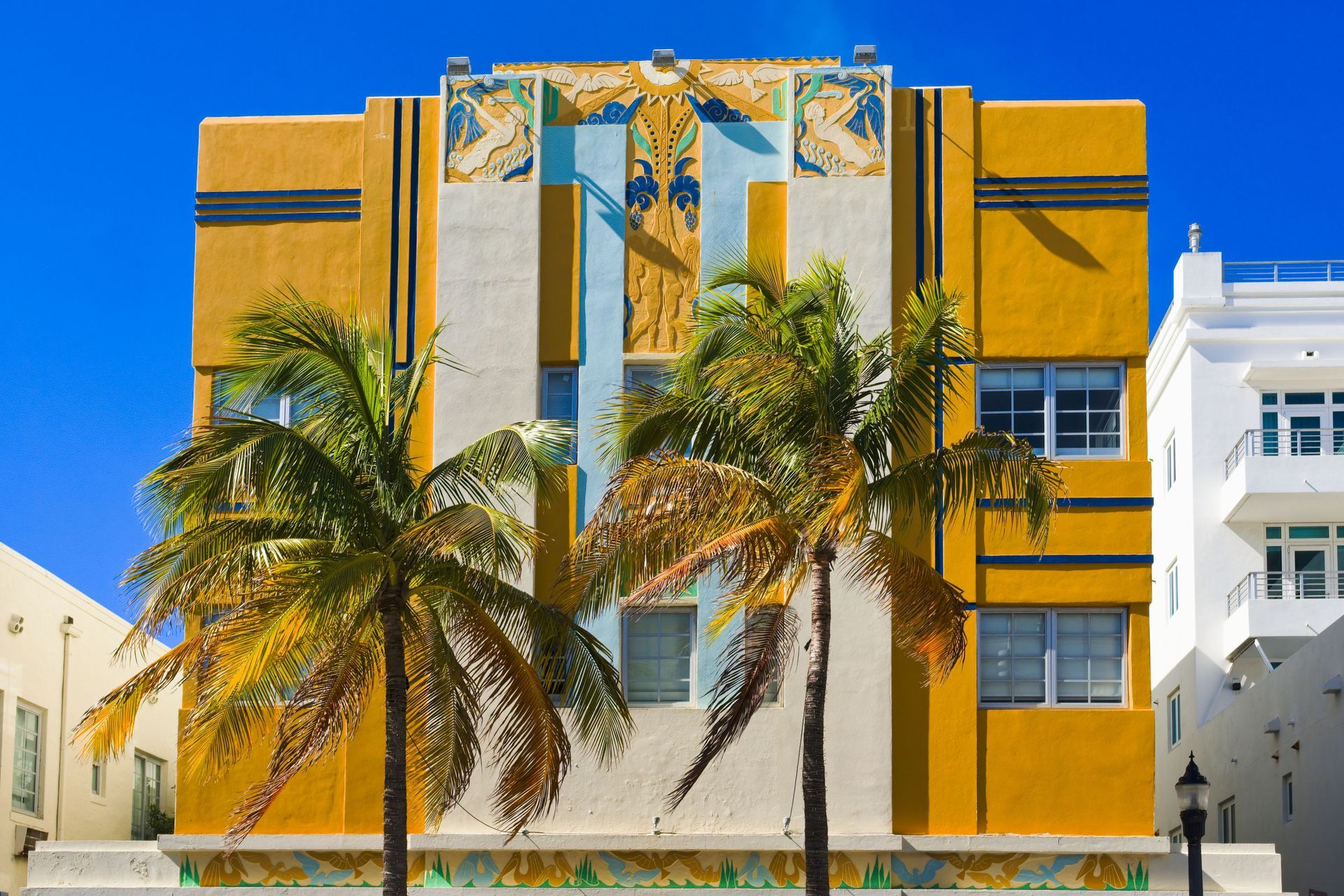 Colorful Art Deco building with palm trees against a bright blue sky