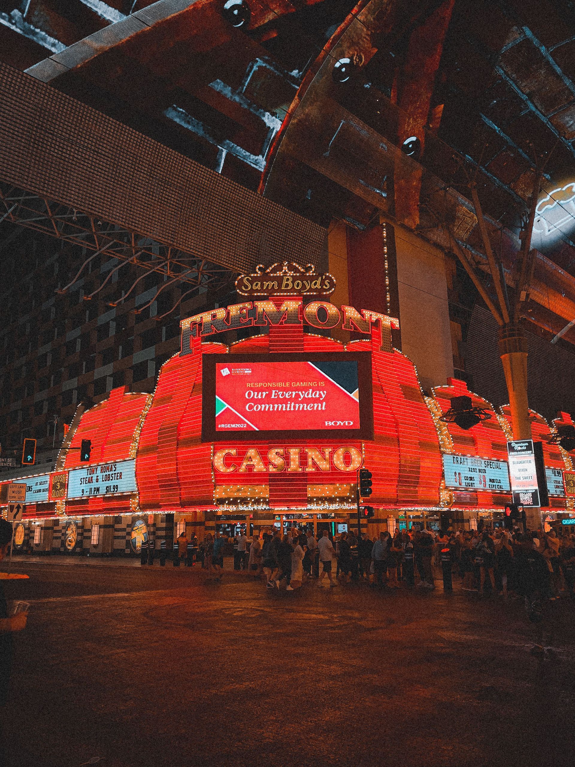 Bright red casino facade at night with glowing signs and a crowd beneath an overhead structure