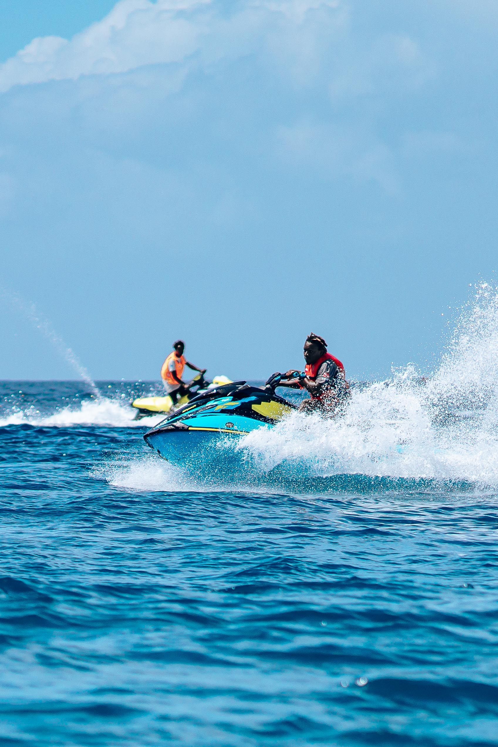 Two people riding a jet ski through blue ocean waves, splashing water under a clear sky