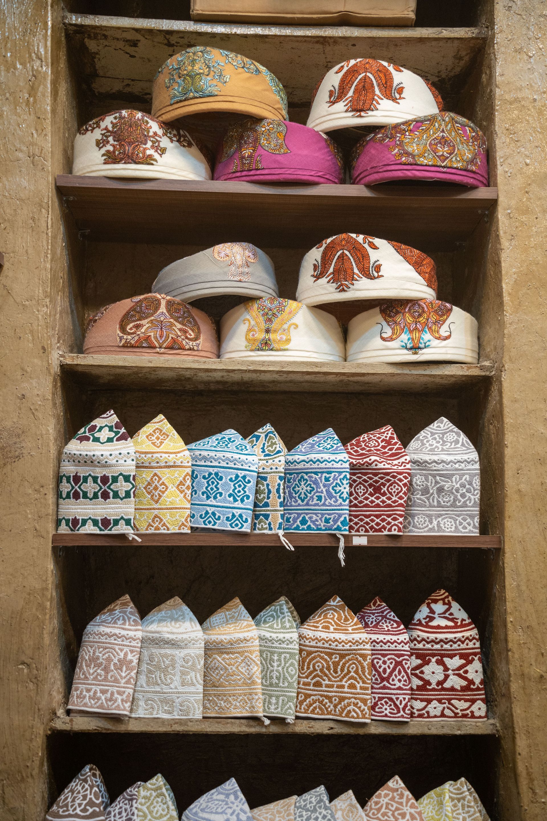 Colorful embroidered caps arranged on wooden shelves in a market stall