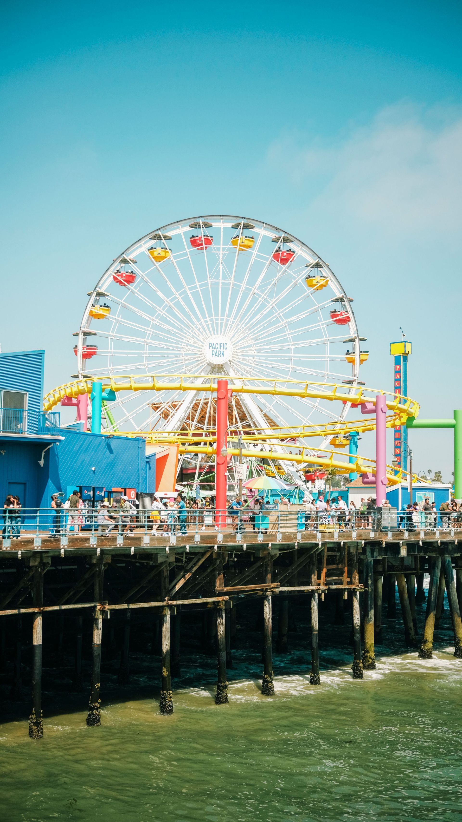 Ferris wheel on a seaside pier with colorful gondolas under a bright blue sky