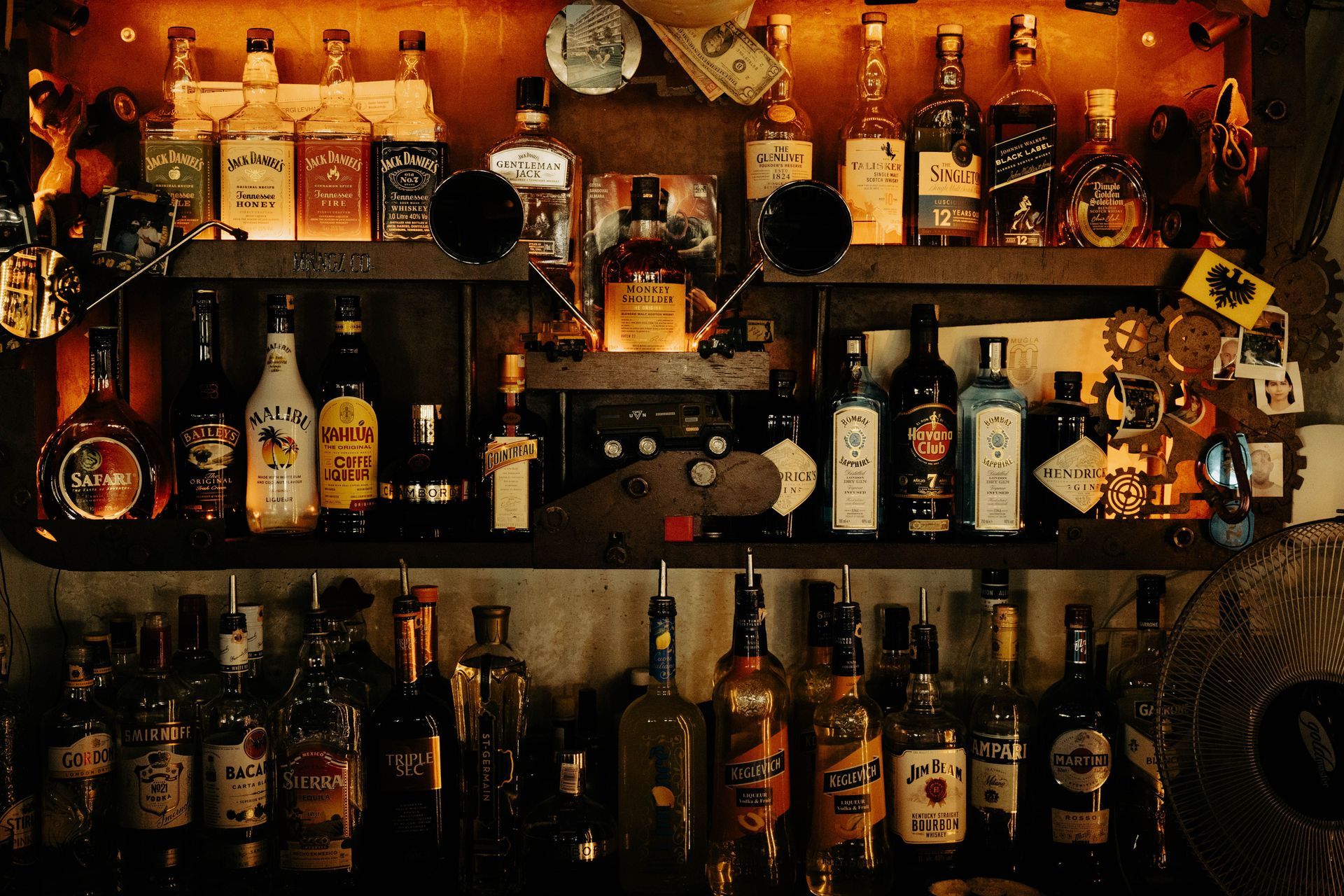 Rows of liquor bottles on wooden shelves in a dimly lit bar.