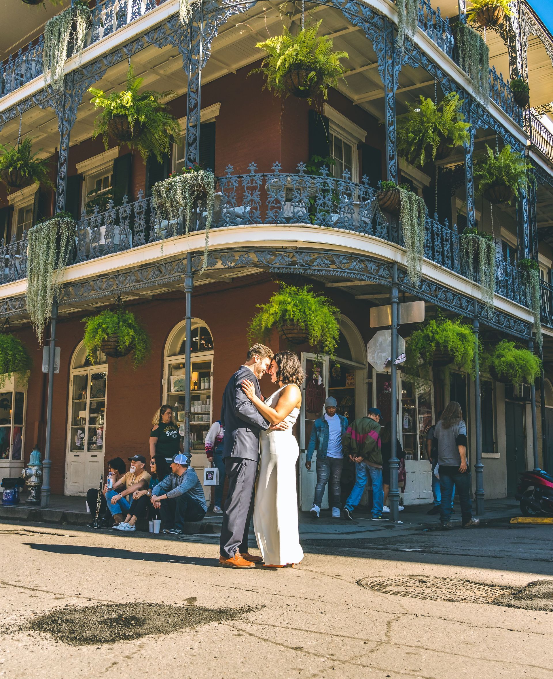 Newlyweds embracing outside a corner building with wrought-iron balconies and hanging greenery