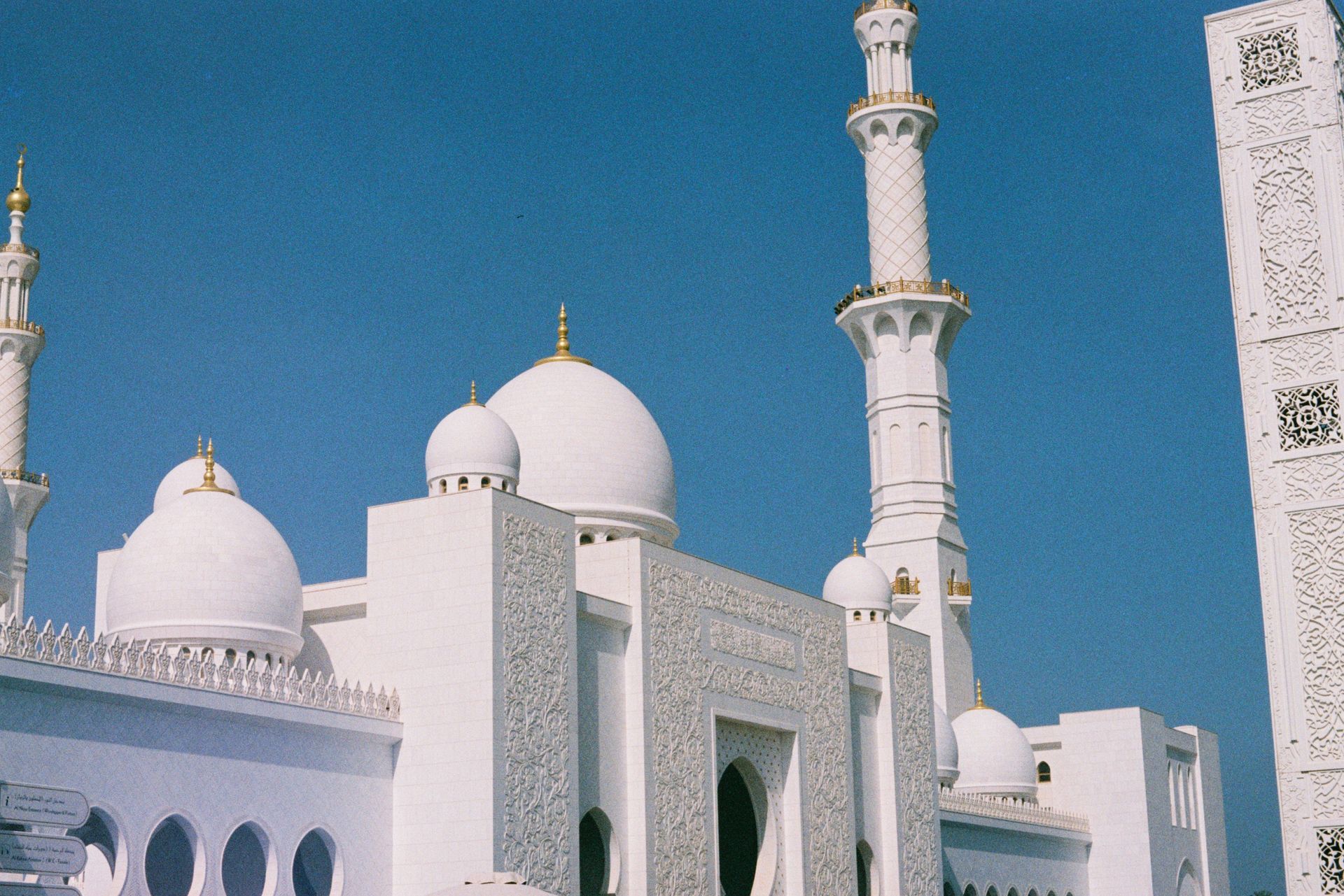 White mosque with domes and a tall minaret against a blue sky