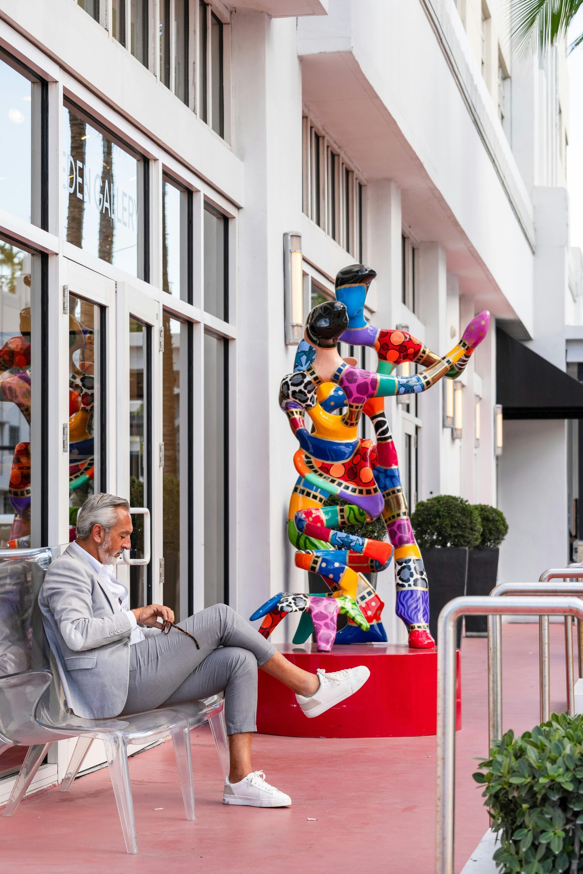 Colorful balloon sculpture beside a seated man on a sidewalk outside a building