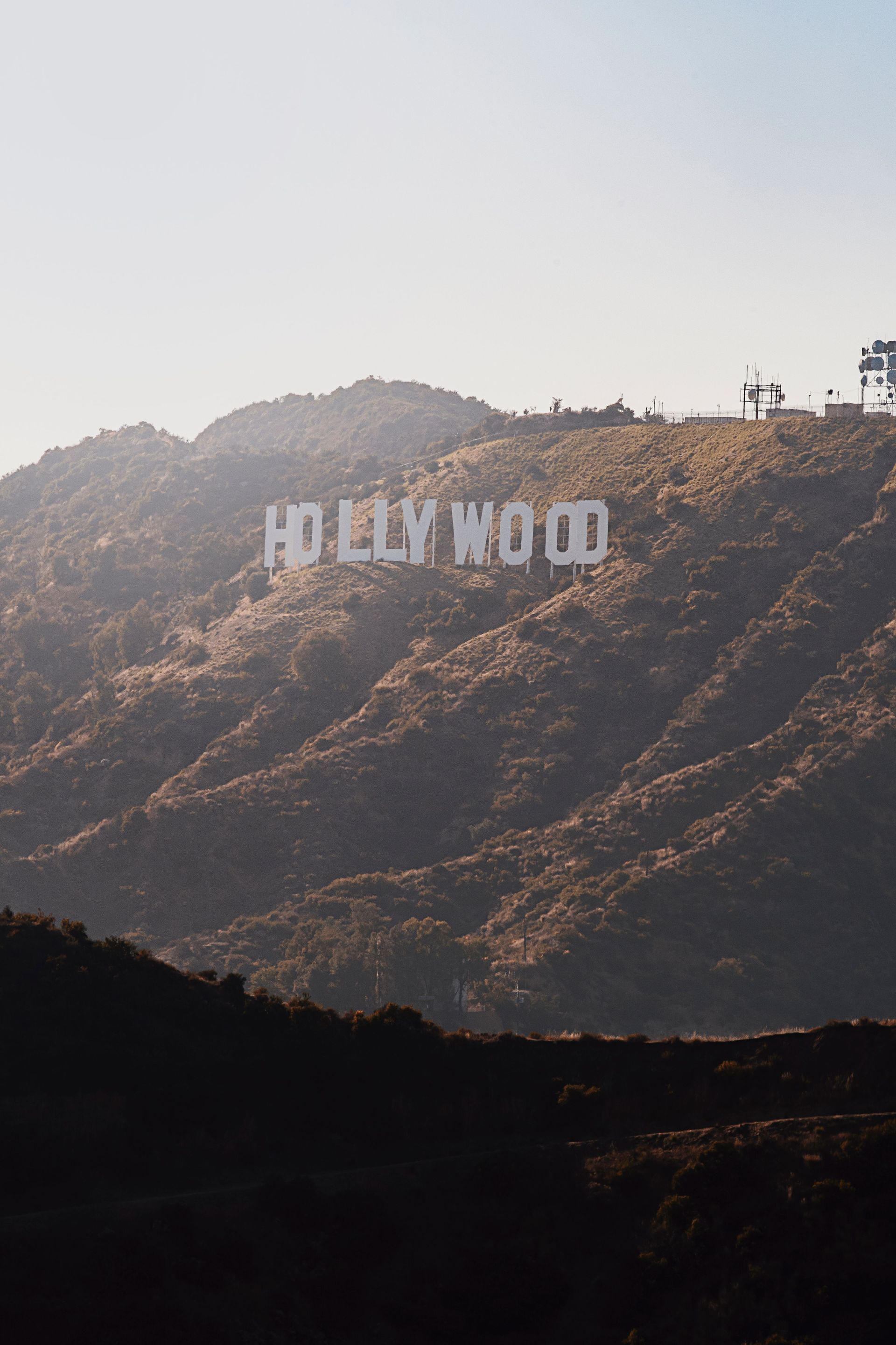 Hollywood sign on a sunlit hillside in Los Angeles, with hazy mountains in the background.