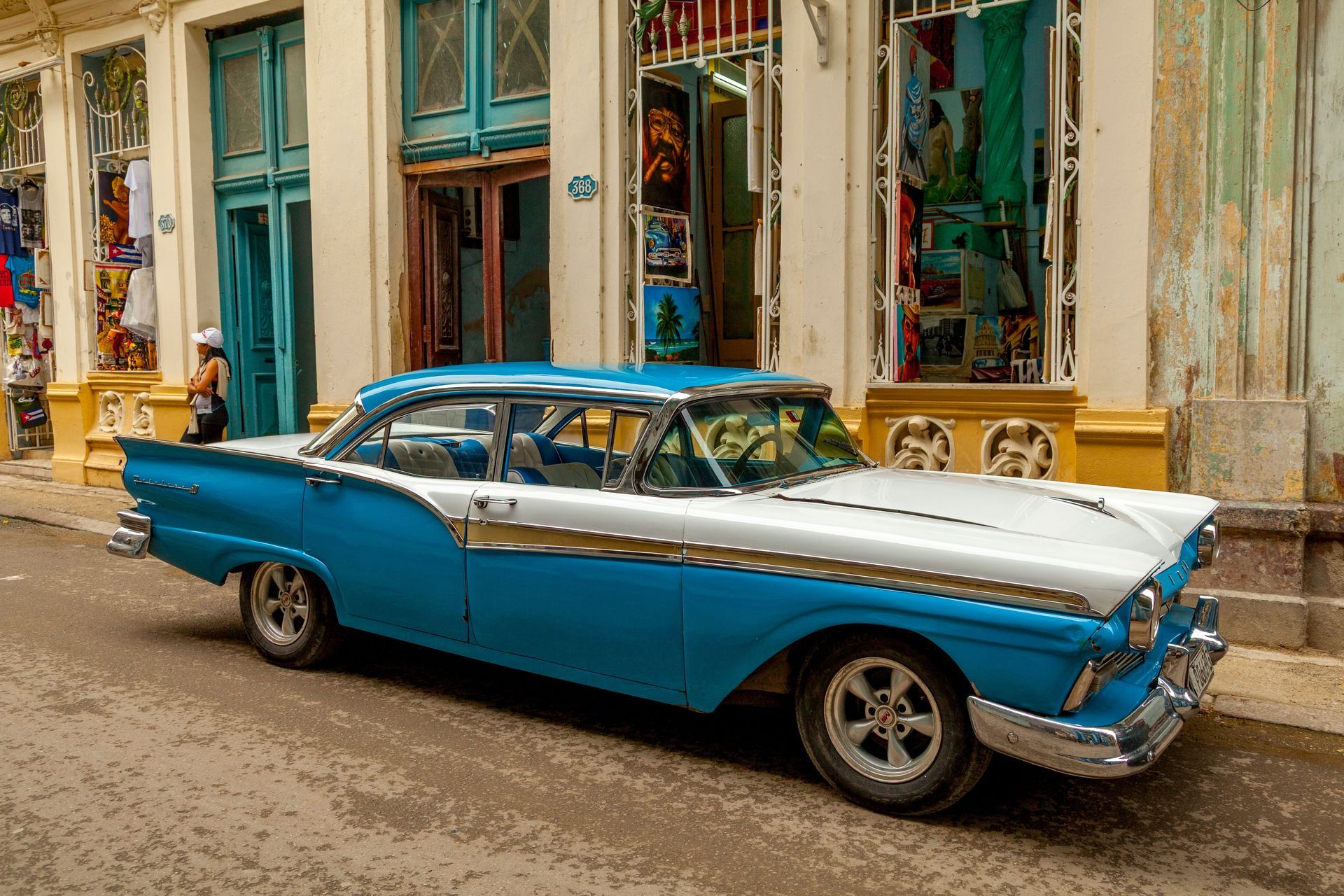 Blue vintage car parked on a colorful street in front of old storefronts