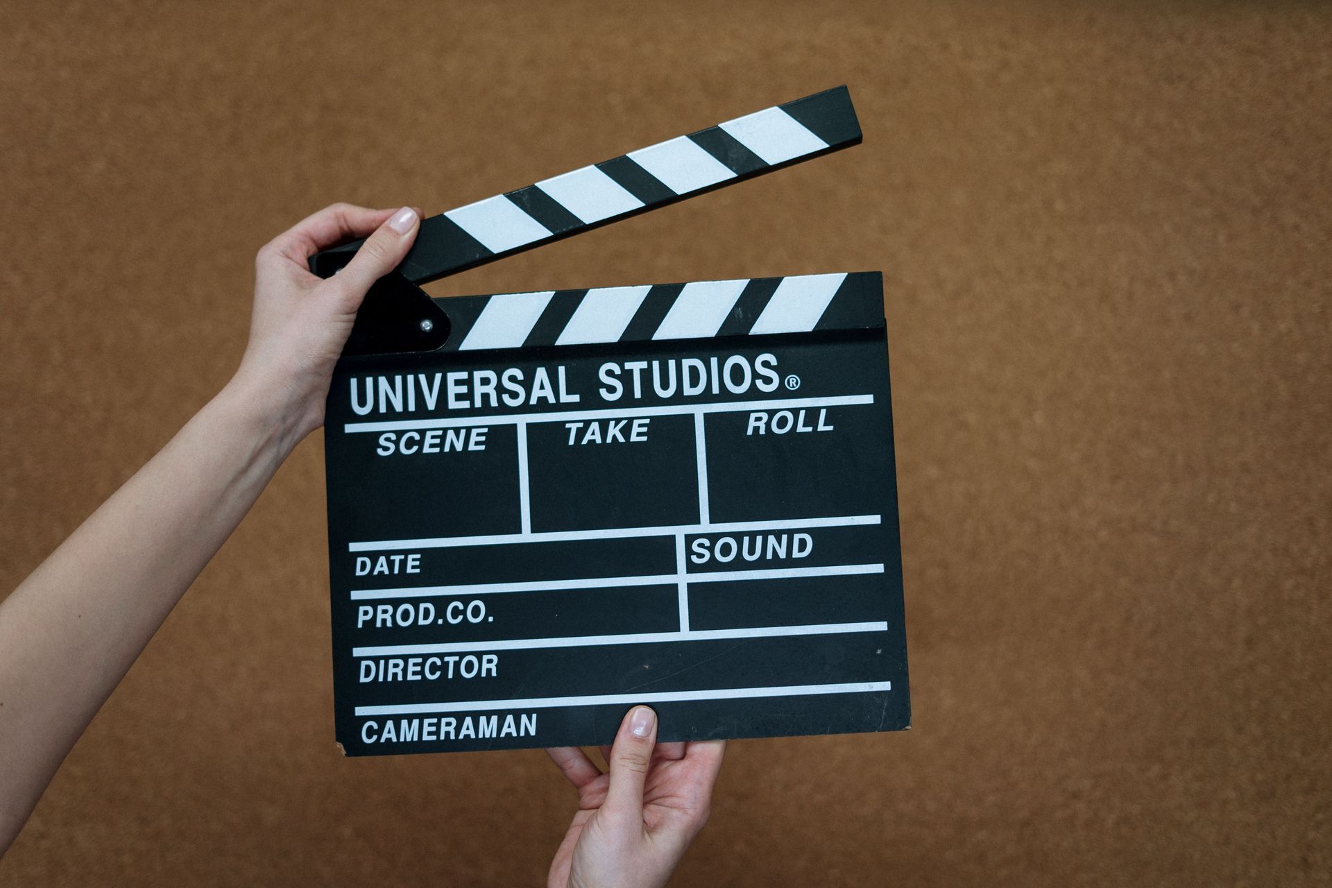 Hands holding a black-and-white film clapperboard against a plain brown background.