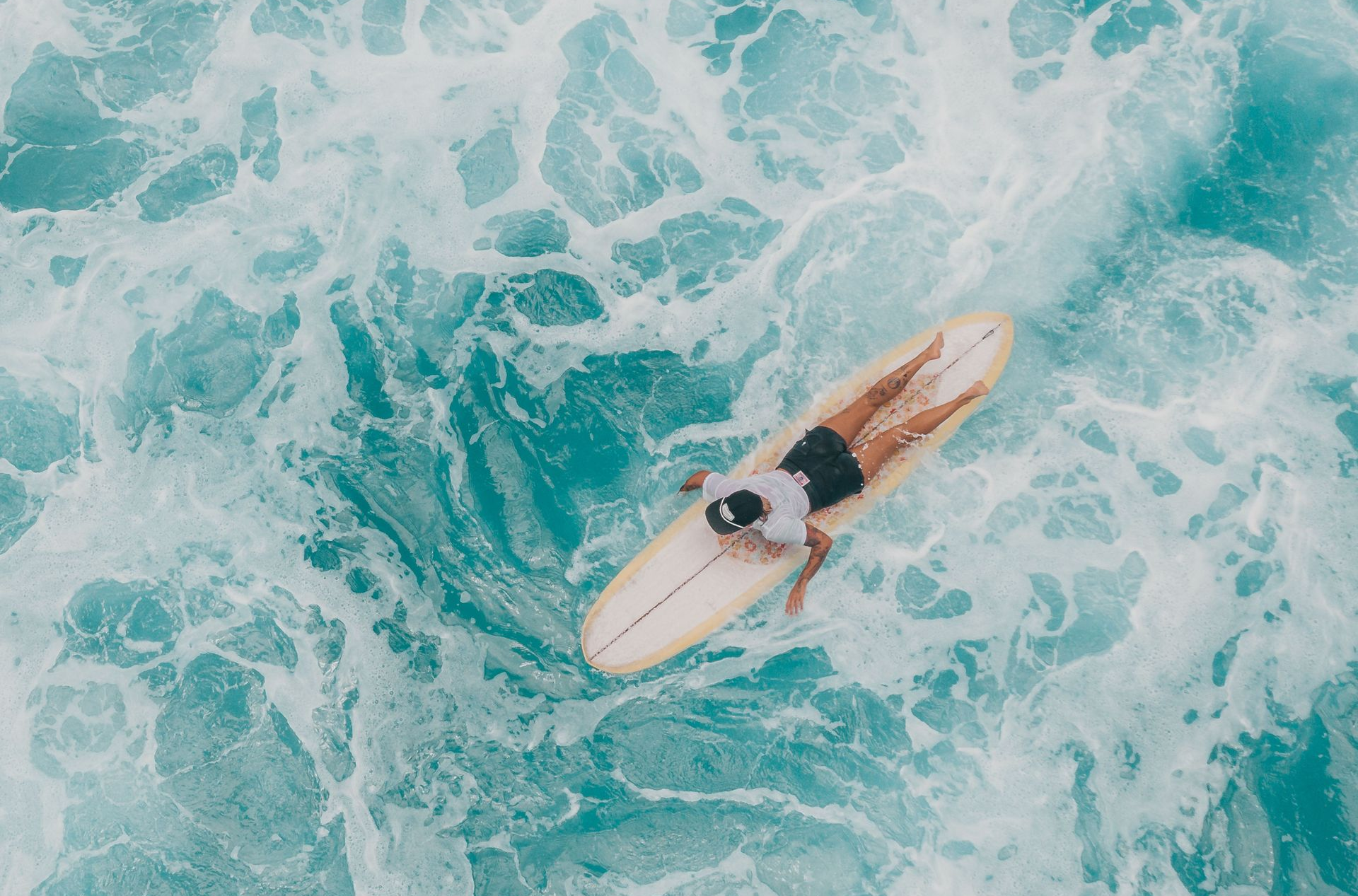 Person on a surfboard in turquoise ocean waves, viewed from above