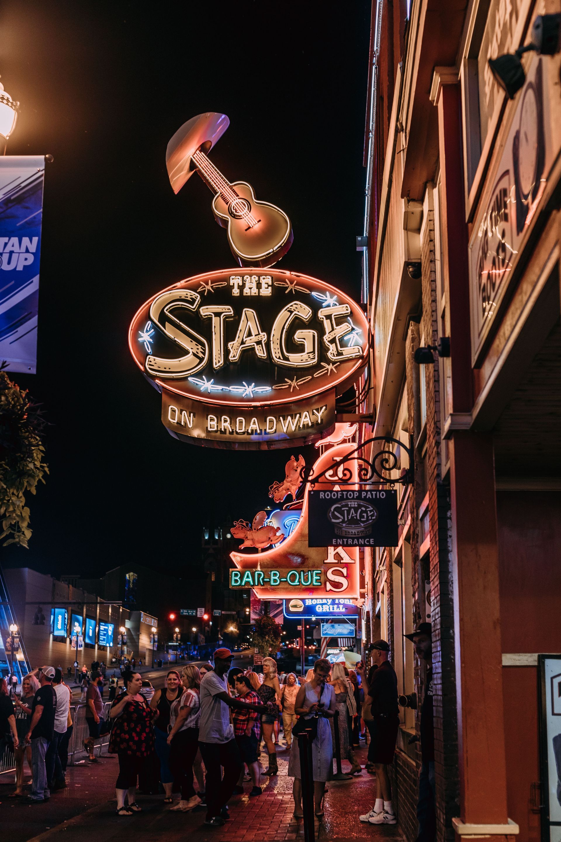 Night street scene with a lit STAG sign and a crowd outside a neon-lit music venue.