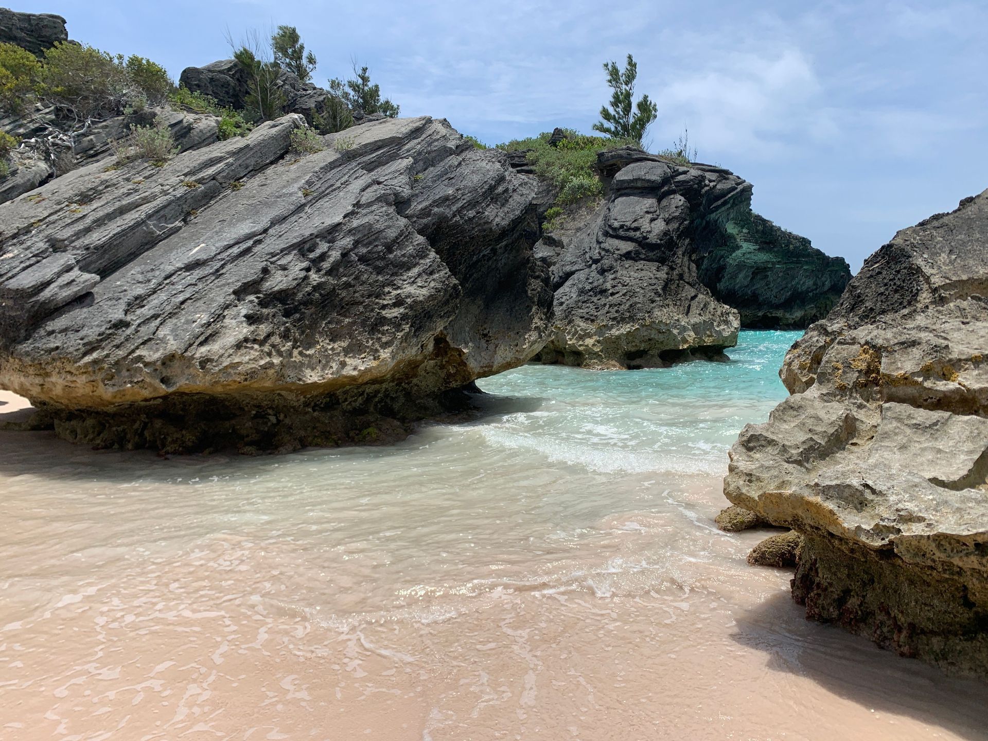 Rocky tropical cove with turquoise water, pale sand, and a blue sky
