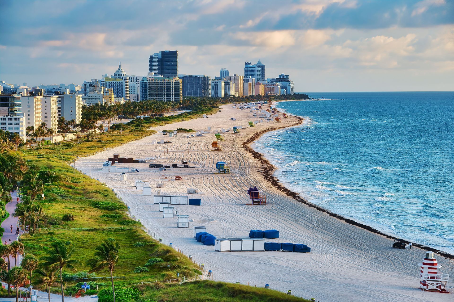 Coastal city beach with turquoise water, white sand, palm trees, and tall buildings along the shore