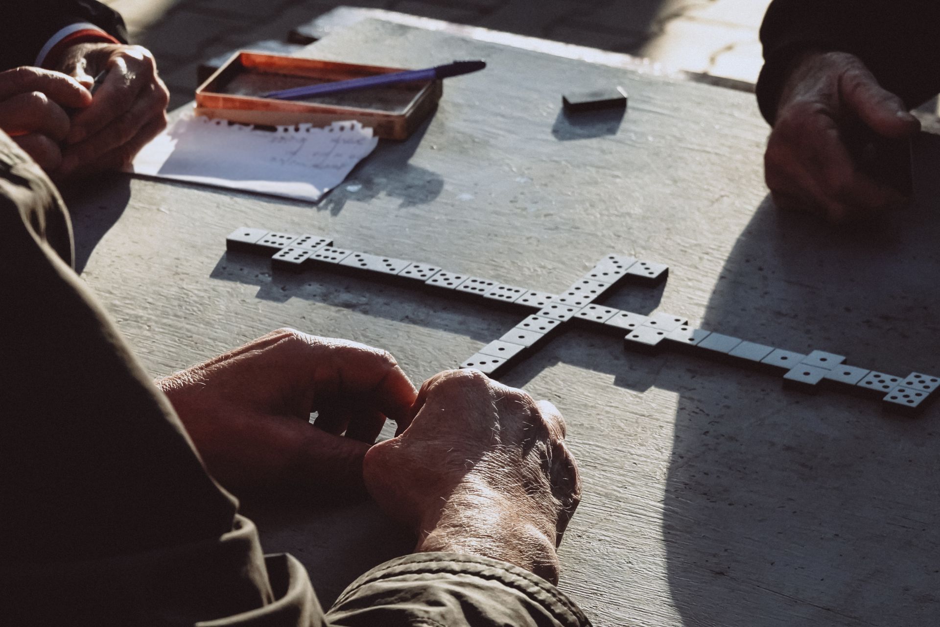 Hands arranging white crossword-style strips on a sunlit table during a board game.