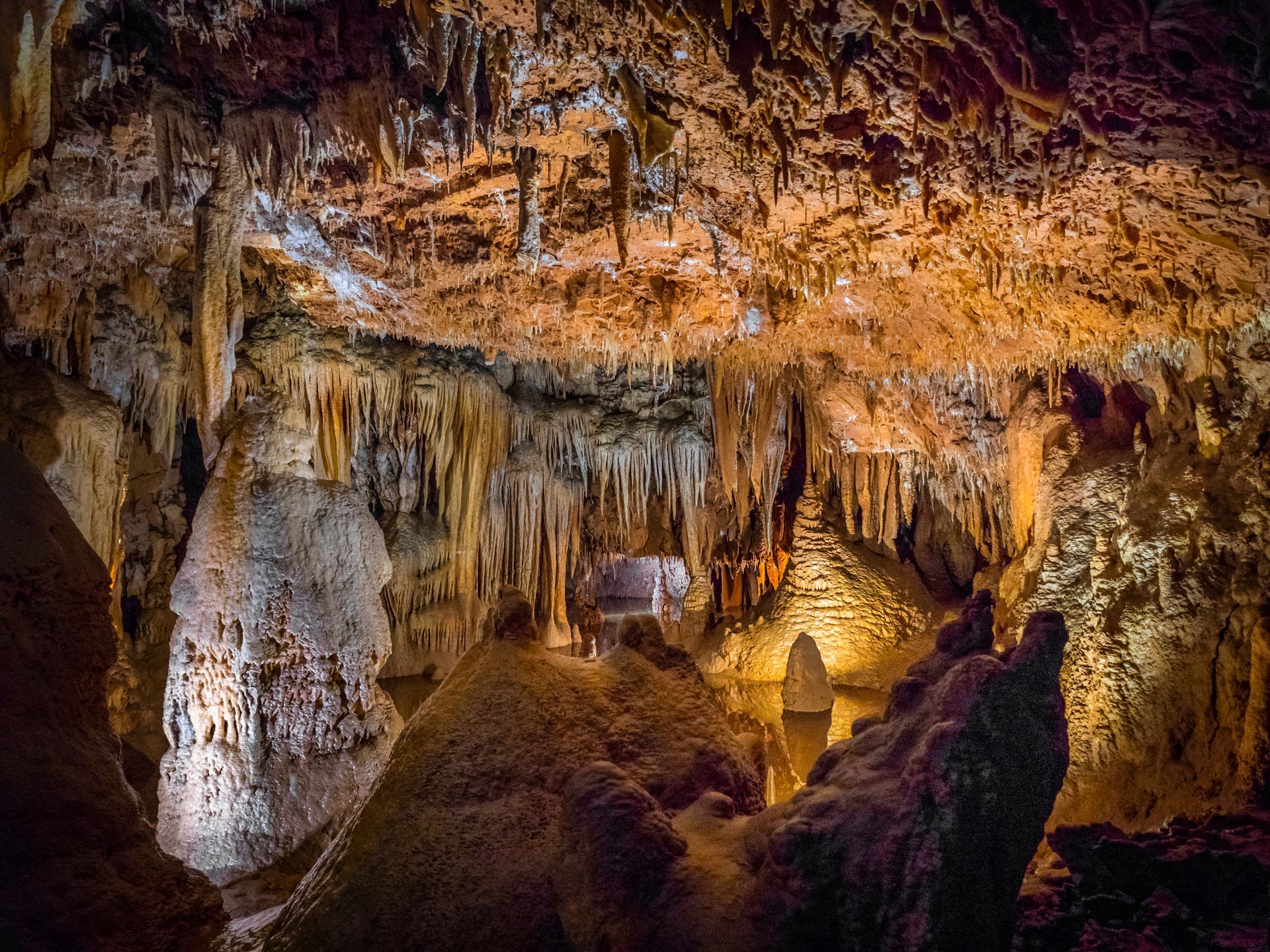 Lit cave interior with stalactites, rocky formations, and warm amber lighting