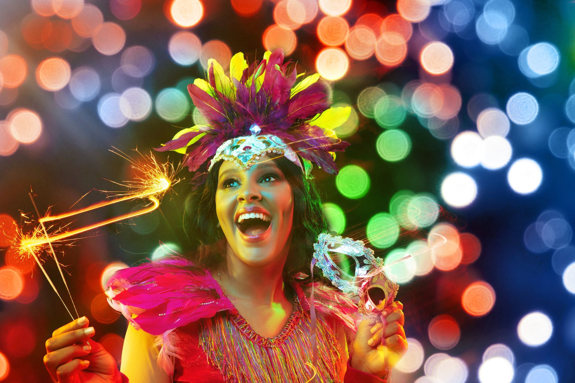 Festive performer in a bright feathered costume smiling amid colorful bokeh lights